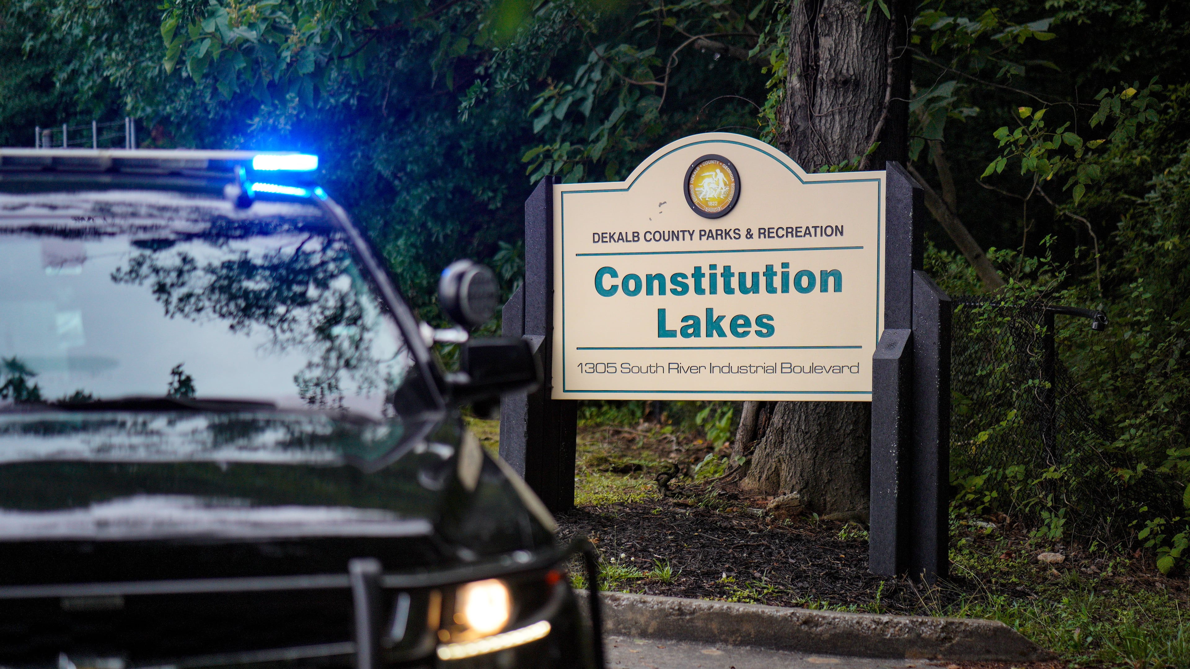 A police cruiser blocks the entrance to Constitution Lakes Park on Friday after a deadly double shooting. (Ben Hendren for the AJC)