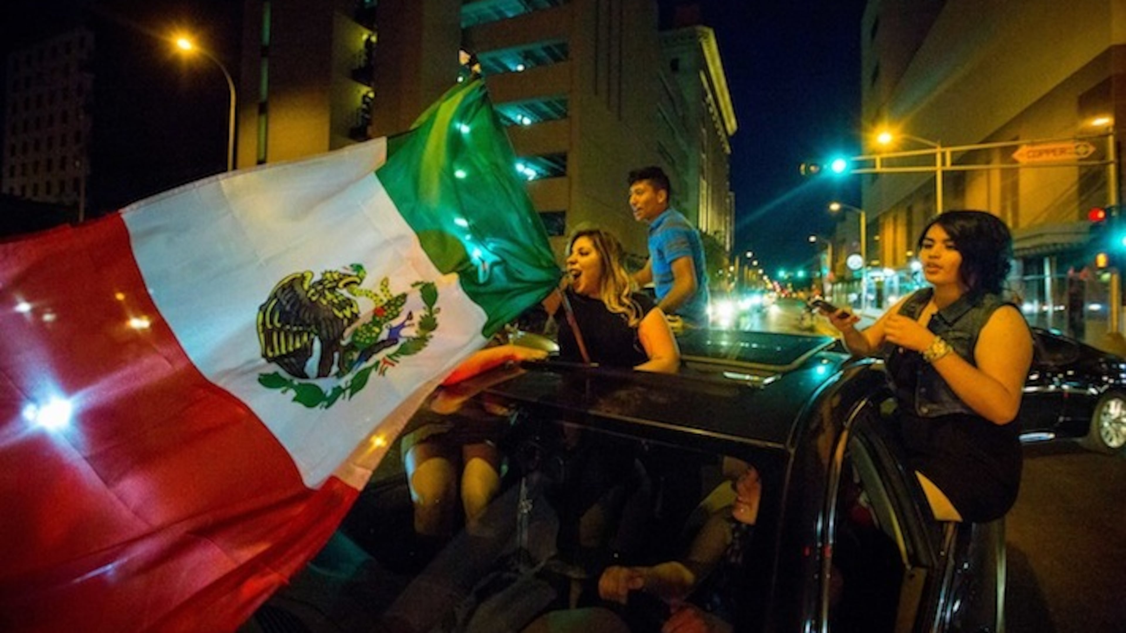 A woman waves the Mexican flag while driving past the Albuquerque Convention Center after a rally by presidential candidate Donald Trump, May 24, 2016.