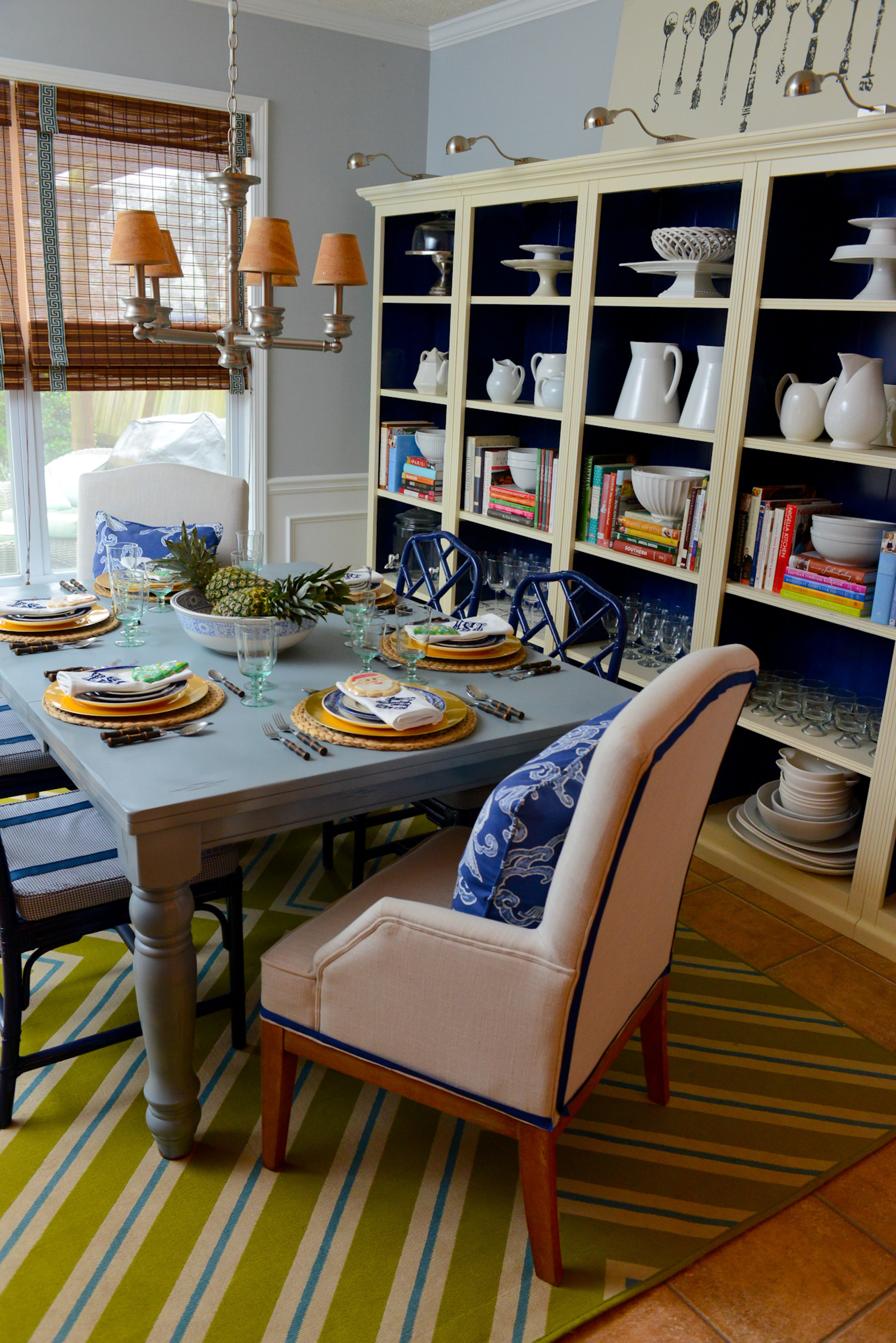 Travis Snyder, an interior designer, repainted an inexpensive dining table a winter gray color to coordinate with the walls. A bright green and blue rug and custom-painted deep blue chairs from Ballard Designs provide vibrant color and anchor the room.