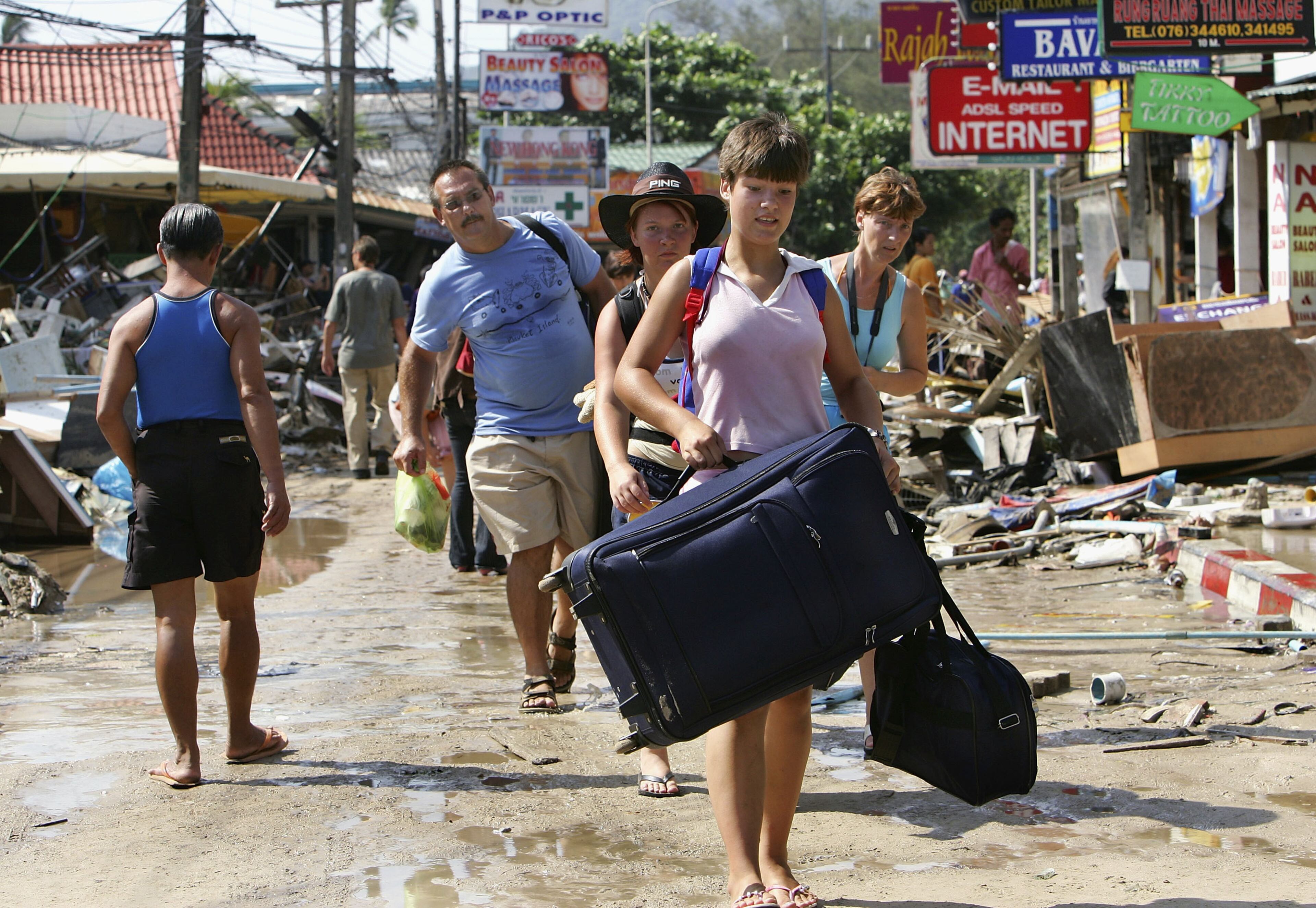PATONG, THAILAND-DECEMBER 27: Foreign tourists walk past devastation, carrying their luggage, as they head to the airport on December 27, 2004 along Patong beach, one of the worst hit provinces of Phuket, Thailand. A 9.0 magnitude earthquake caused a Tsunami wave to hit the coastal areas of South East Asia killing more than 16,000, with thousands still missing. (Photo by Paula Bronstein/Getty Images)