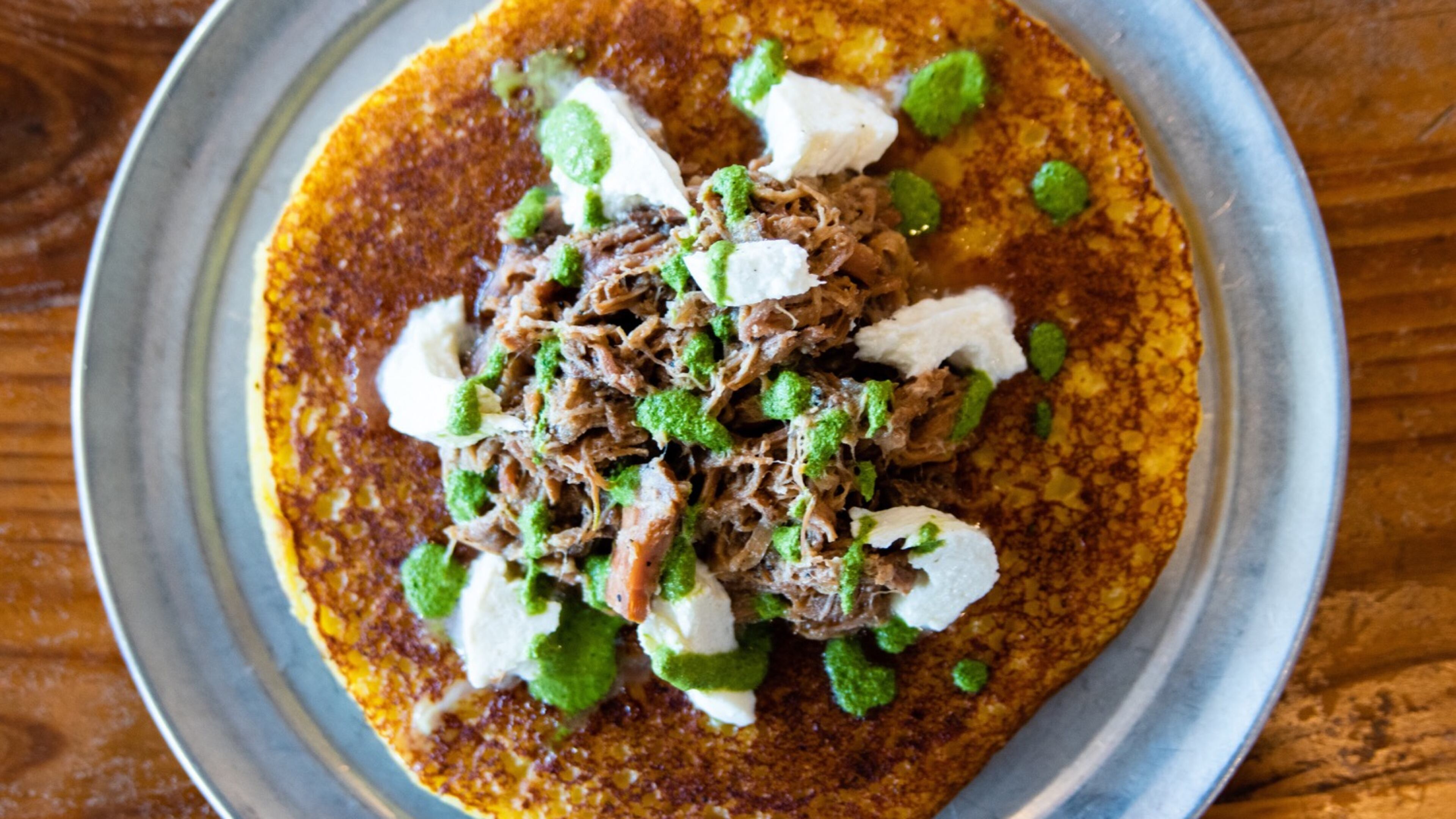 The cachapa pernil at Arepa Mia is topped with roasted pork cooked in mojo sauce, caramelized onion, cilantro and guayanes cheese.