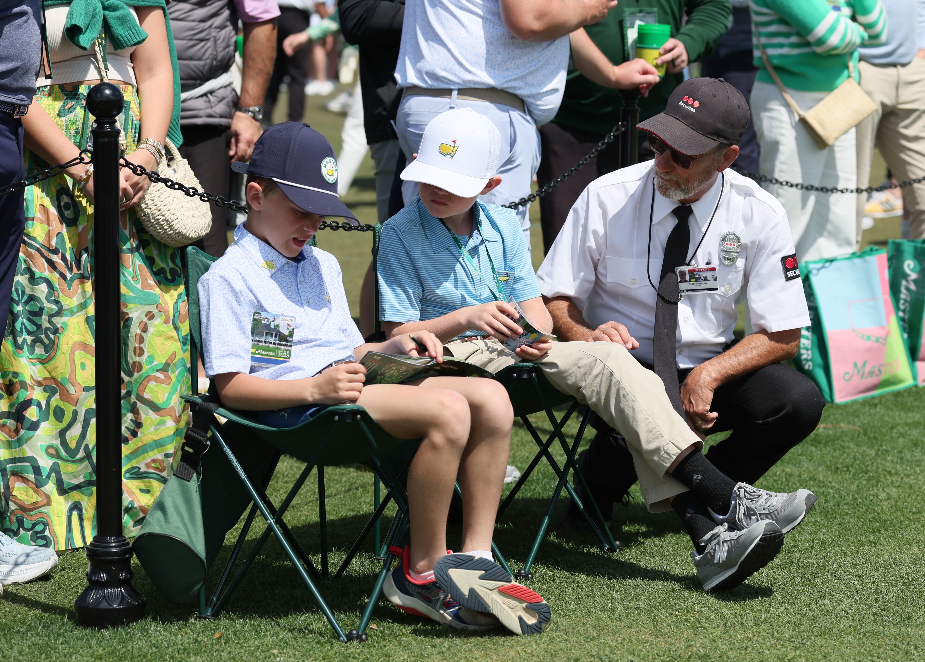 Security guard Gary Herman chats with friends Wyatt Claxton, left, and Asher Marsh, 10, both from Statesboro, GA, inside the ropes at the practice putting green during third round of the Masters golf tournament, at Augusta National Golf Club, Saturday, April 12, 2025, in Augusta, Ga. (Jason Getz / AJC)