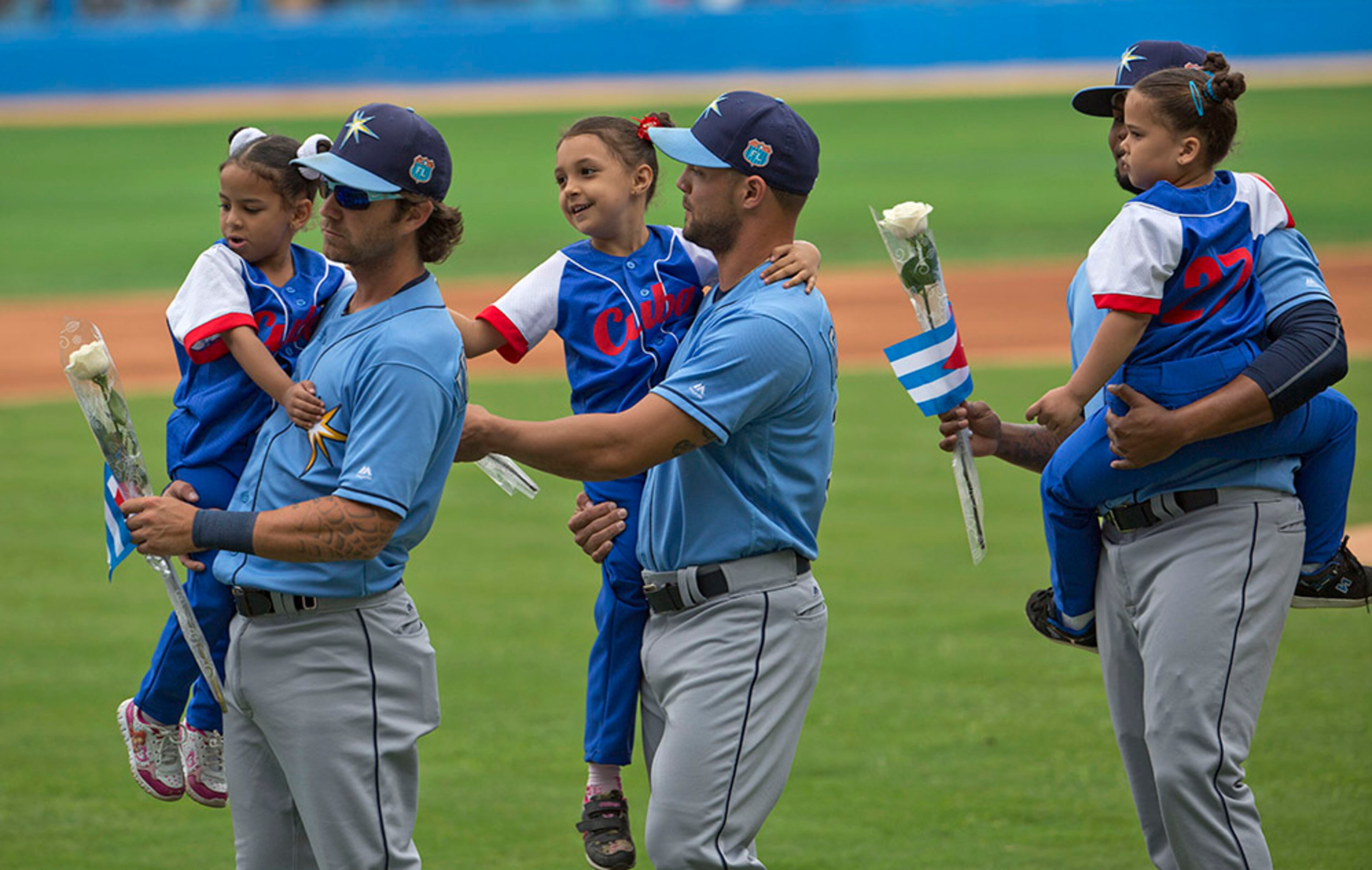 Members of the Tampa Bay Rays carry children and flowers before an exhibition baseball game between the Tampa Bay Rays and the Cuban National team at the Estadio Latinoamericano, Tuesday, March 22, 2016, in Havana, Cuba, that President Barack Obama and Cuban President Raul Castro attended.