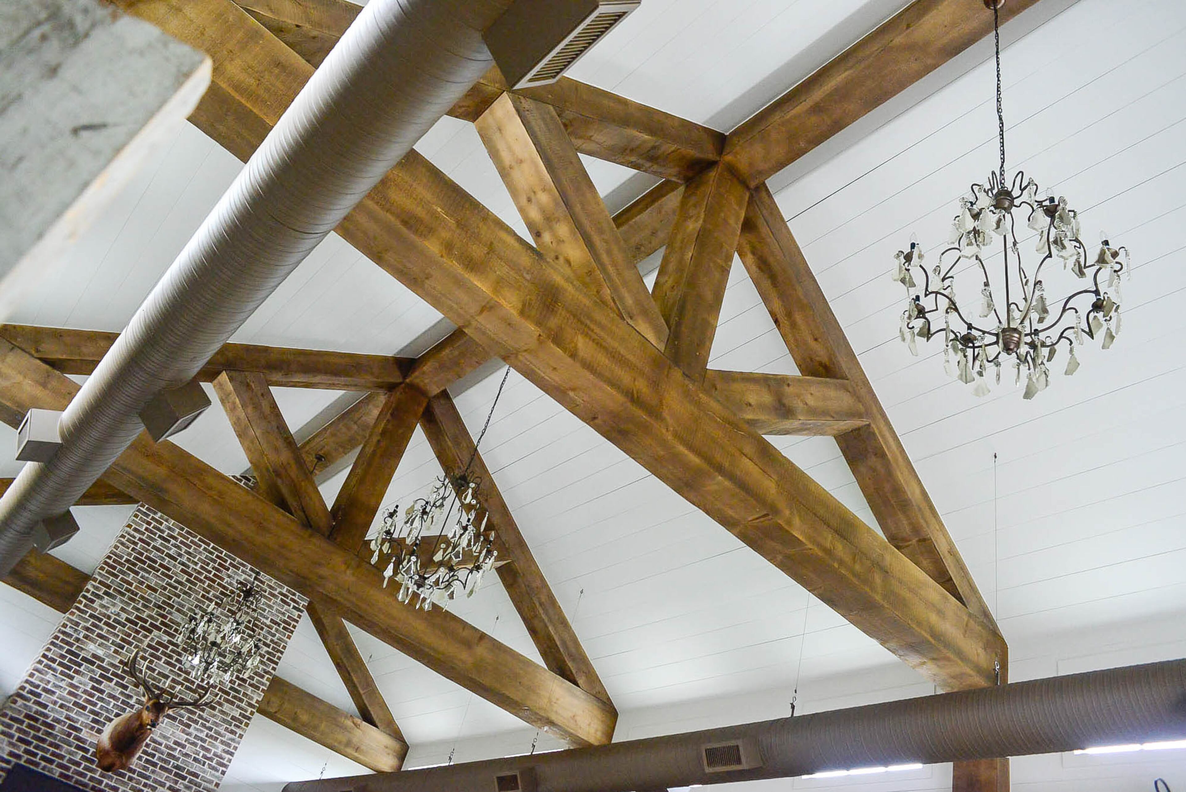Massive wooden beams in the "party barn" accentuate the spacious guest house and crystal chandeliers from RH bring city glam to the farmhouse-style structure.