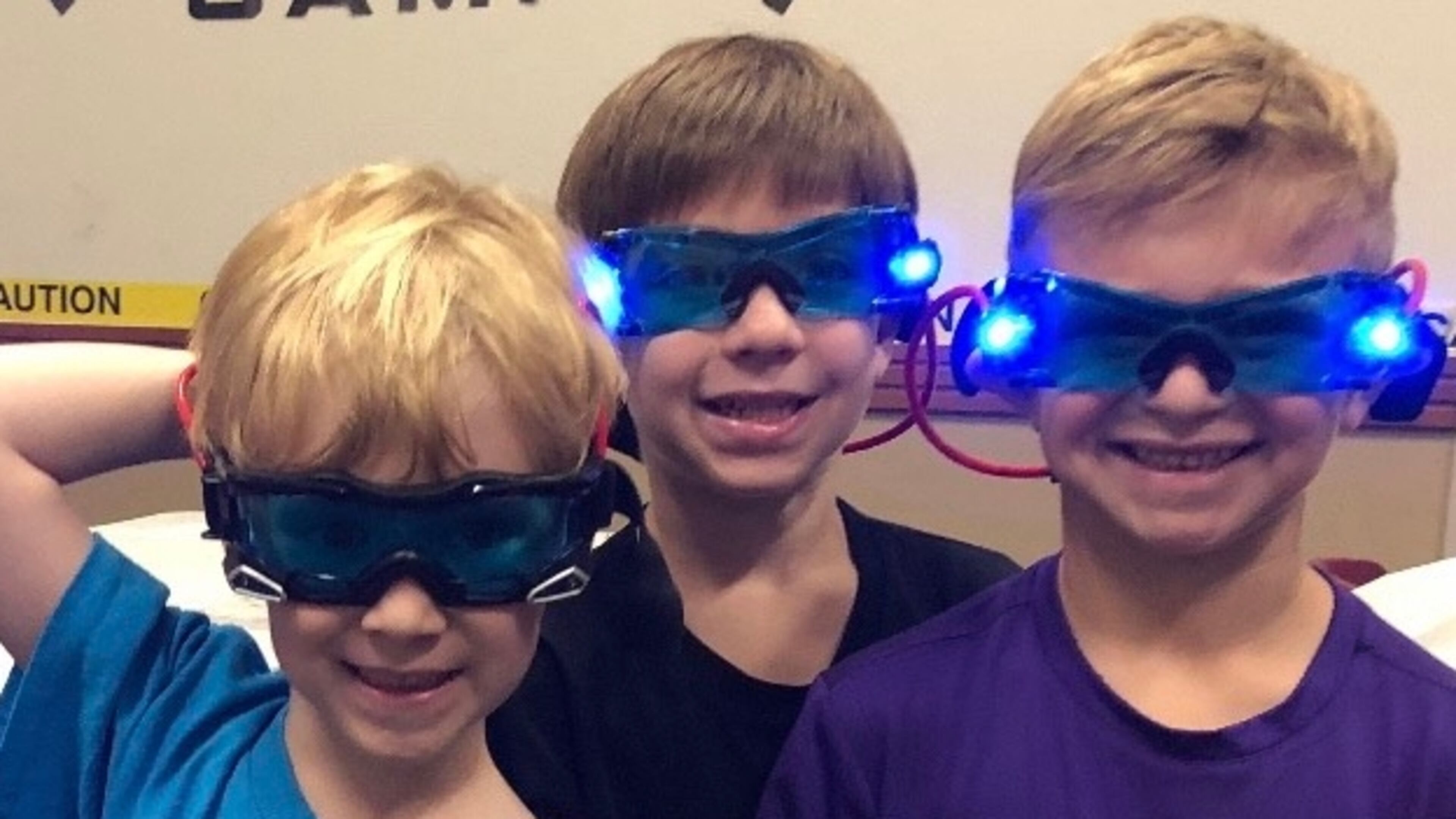 MJCCA Day Camps Spy Camp campers smile proudly after completing a spy course through a darkened room using their night vision goggles. (L-R: Daniel Kellner, Dylan Sonenshine and Jaron Coplin).