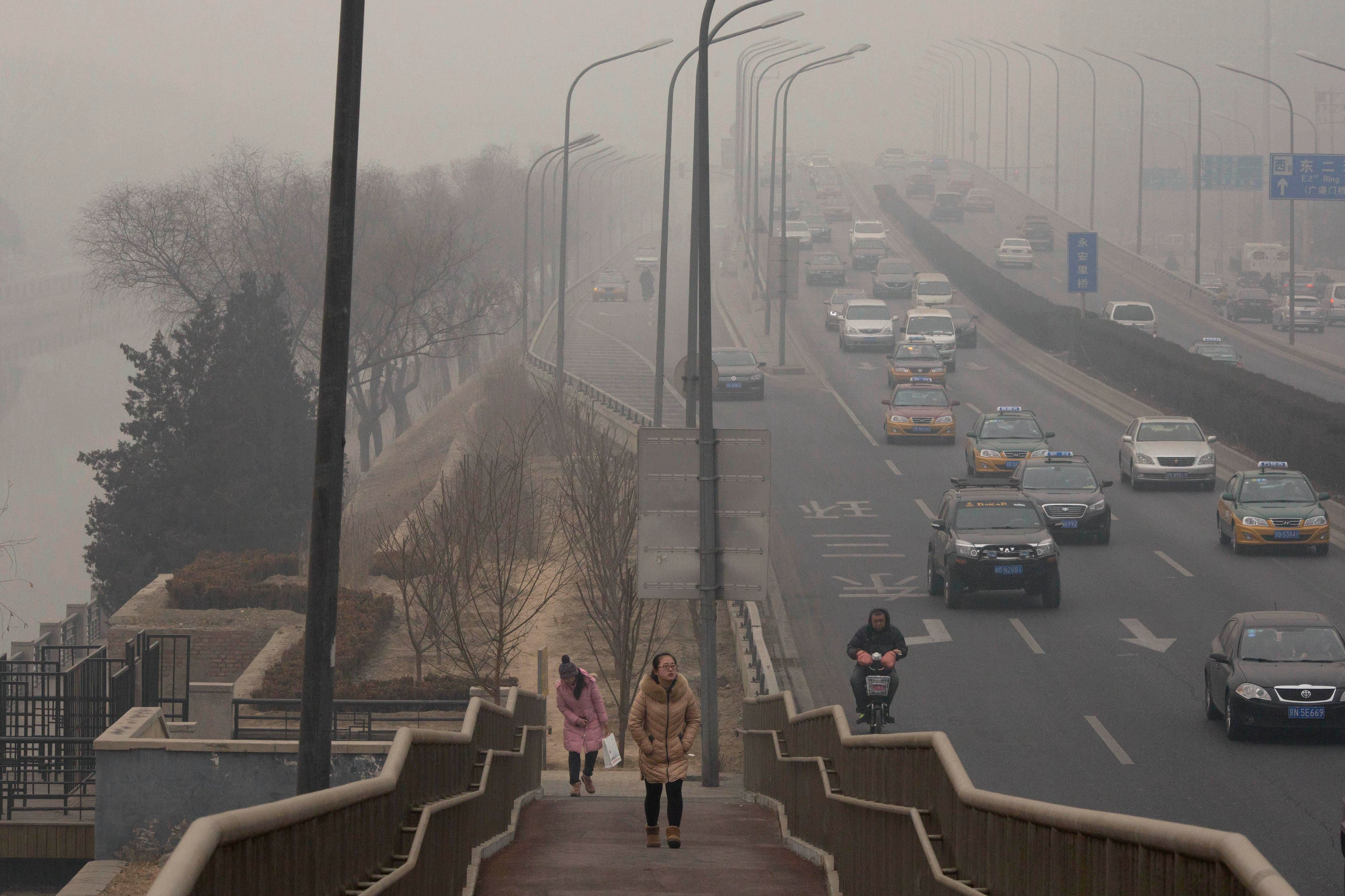 Women walk up an overpass near a highway during a hazy day in Beijing, China, Wednesday, Feb. 26, 2014. Beijing remained cloaked in hazardous white pollution hiding much of its skyline Wednesday, despite the announced closures or production cuts at 147 of the city's industrial plants.