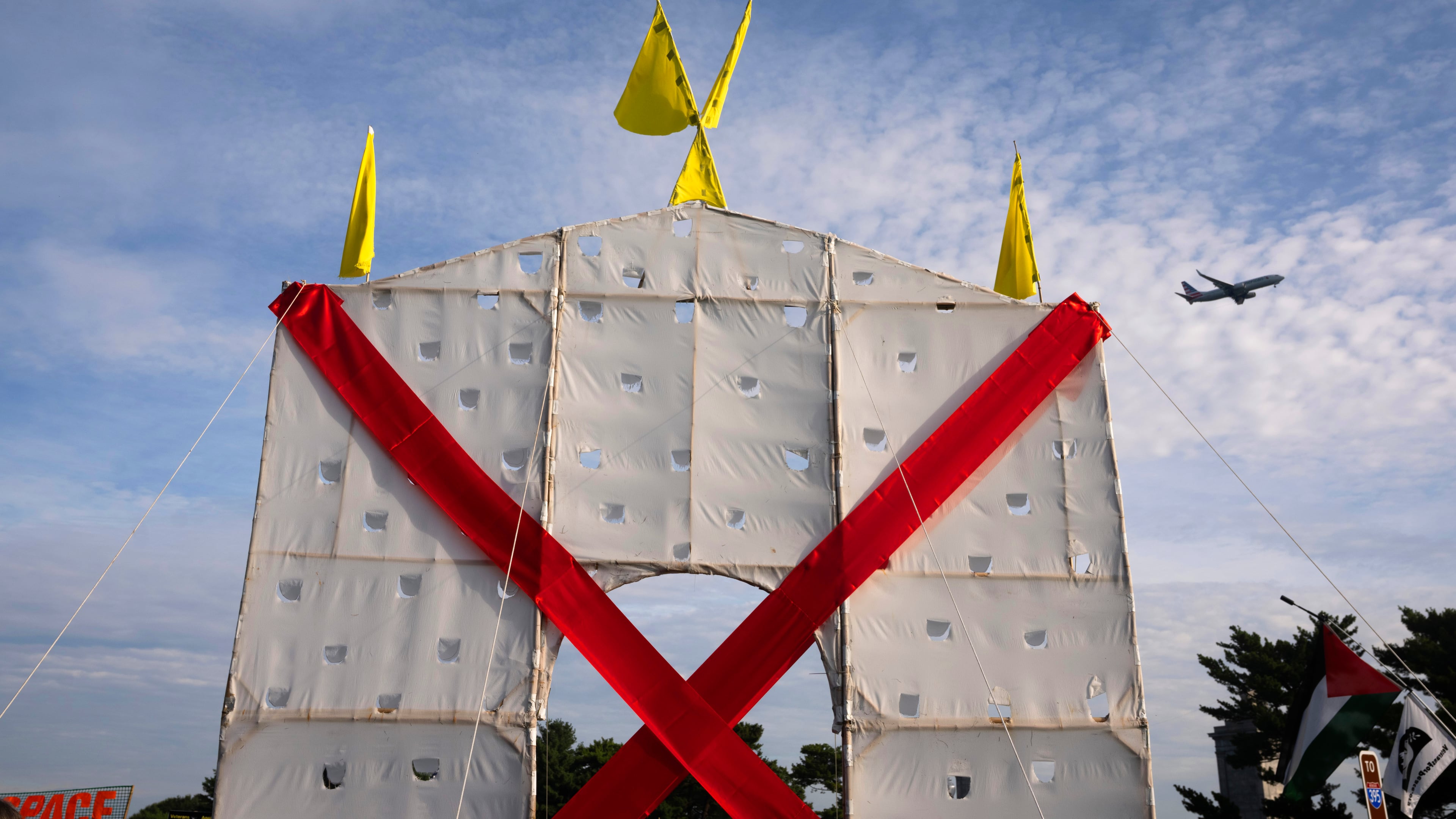A plane flies over an anti-arch structure lifted up by demonstrators at Memorial Circle to protest the proposed Triumphal Arch, Thursday, Oct. 1, 2026, in Arlington, Va. (AP Photo/Allison Robbert)