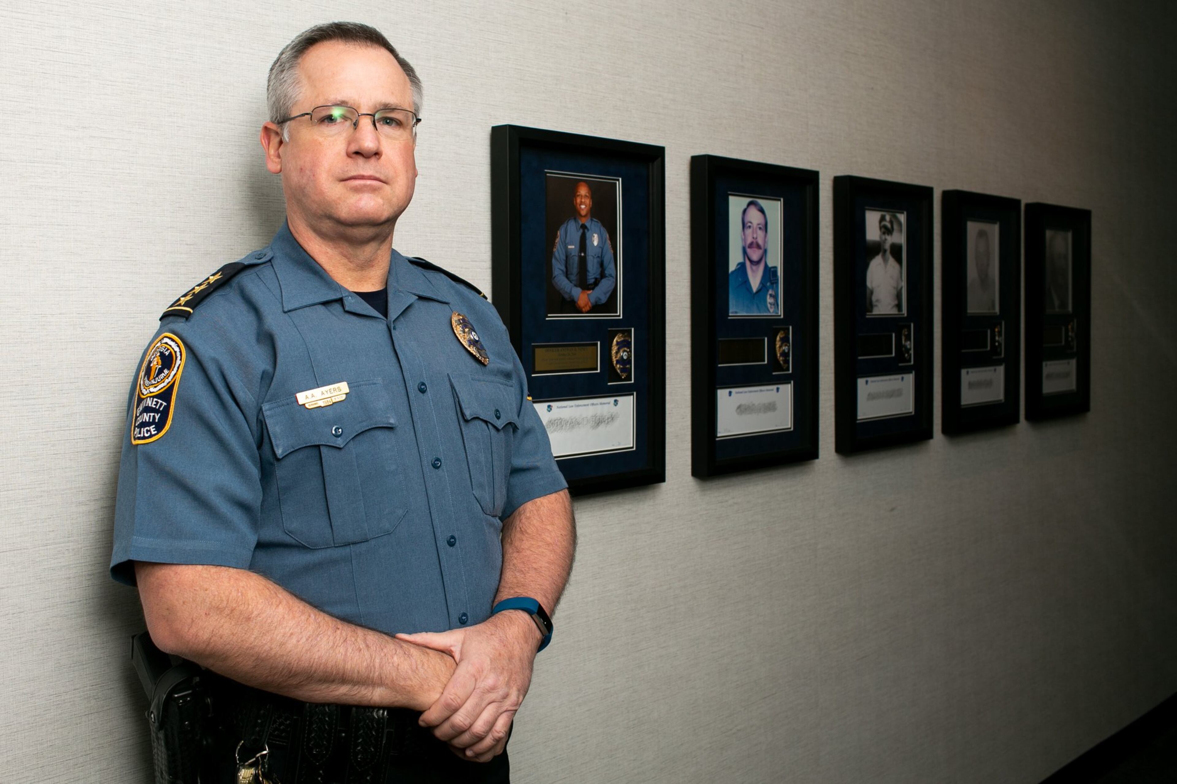 Now-former Gwinnett County police Chief Butch Ayers poses with memorials of the five officers who lost their lives in the line of duty at the Gwinnett County Police headquarters in Lawrenceville. Ayers retired Nov. 15, after five years in charge and more than three decades with the department. (Photo/Rebecca Wright for the Atlanta Journal-Constitution)