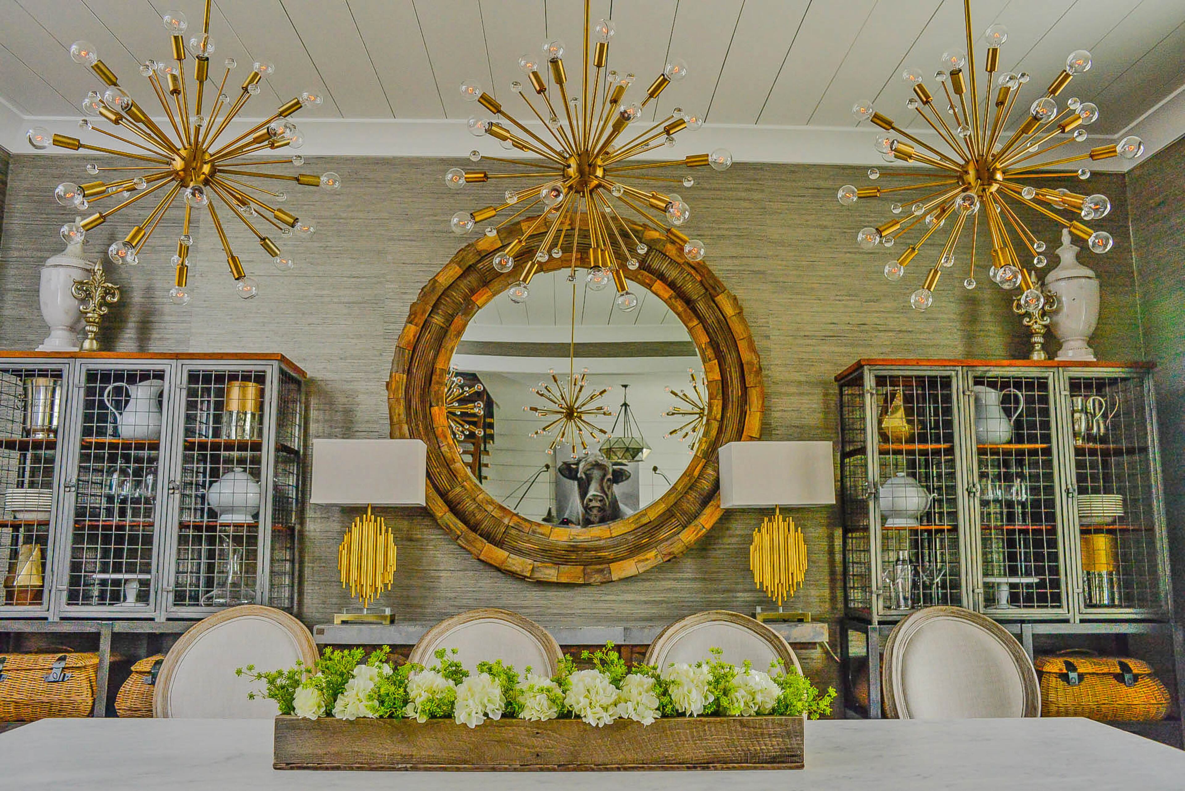 Three glass and brass chandeliers hang over the Carrara marble dining table. The giant circular wood frame mirror reflects the bull canvas print in the sitting room.