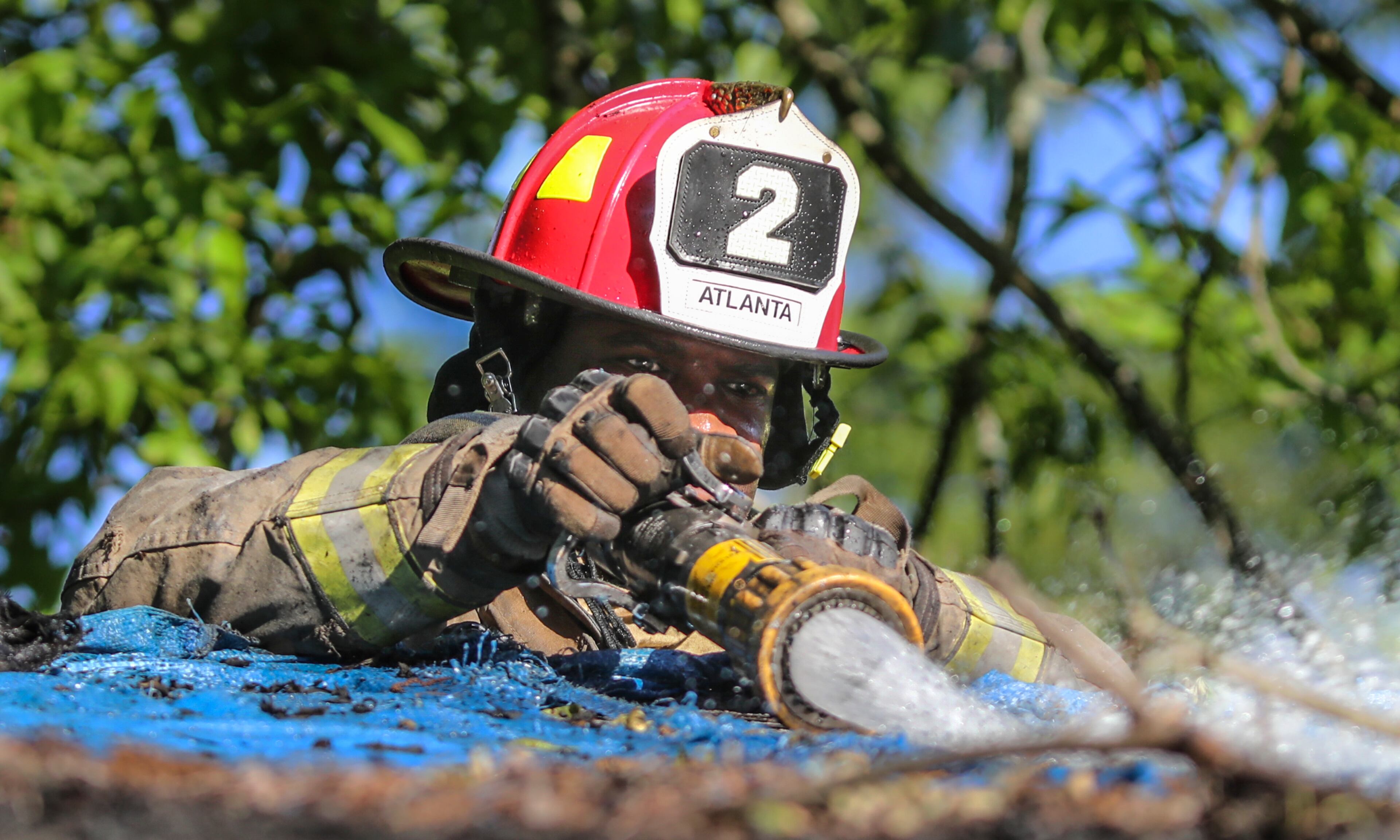 Atlanta Fire Rescue Lt. Matthew Brown hits hot spots on the roof as officials investigate a house fire Thursday in southwest Atlanta. JOHN SPINK / JSPINK@AJC.COM