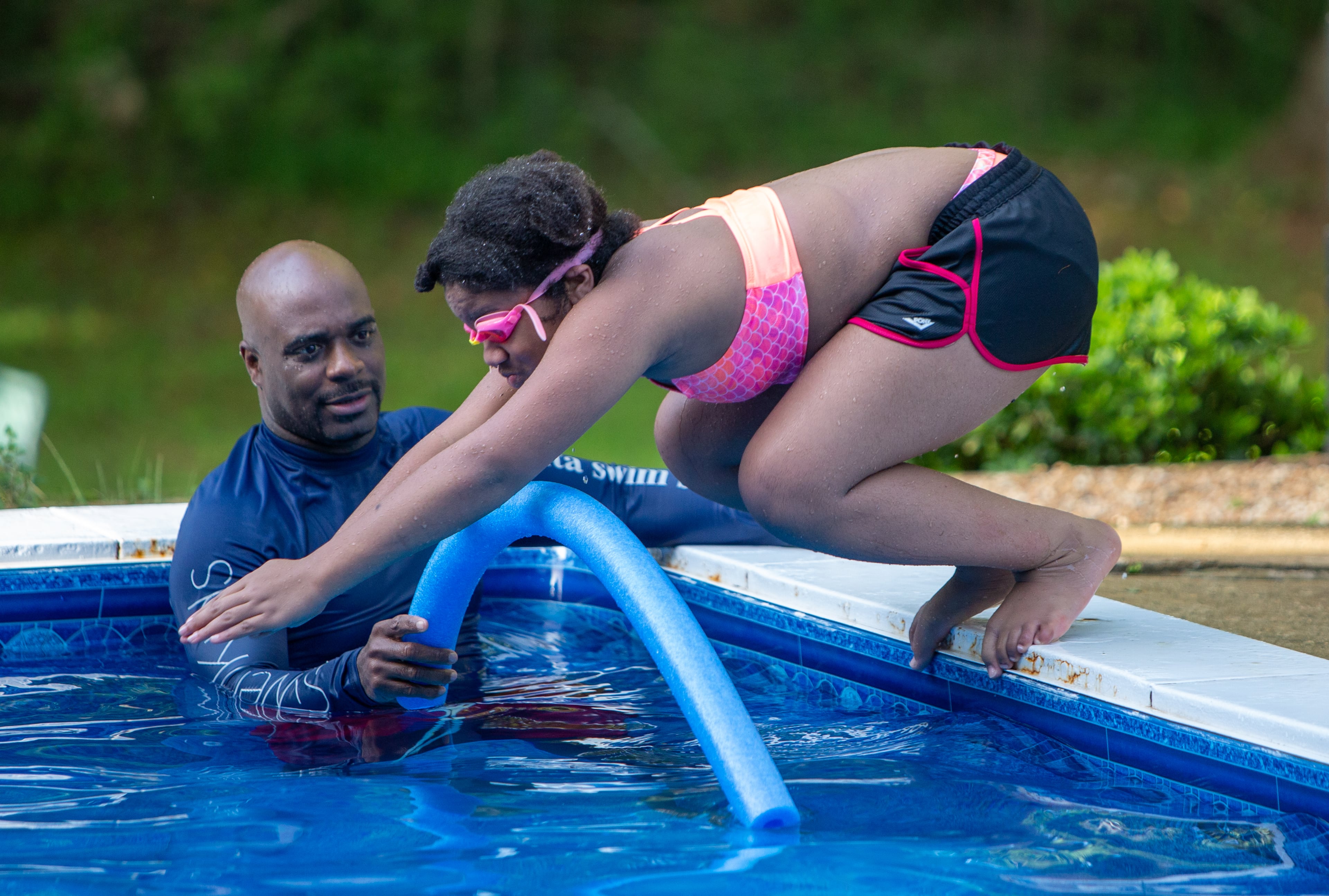 SwemKids instructor Ezra Jones watches Honesty Mincey (age 11) dive (CQ according to organizer). After COVID shuttered pools, a Fayetteville man offered his backyard pool for swimming instruction & water safety lessons to Atlanta city kids. SwemKids is a nonprofit that offers free swimming gear & lessons as an in-school program for kids in low income neighborhoods. PHIL SKINNER FOR THE ATLANTA JOURNAL-CONSTITUTION.