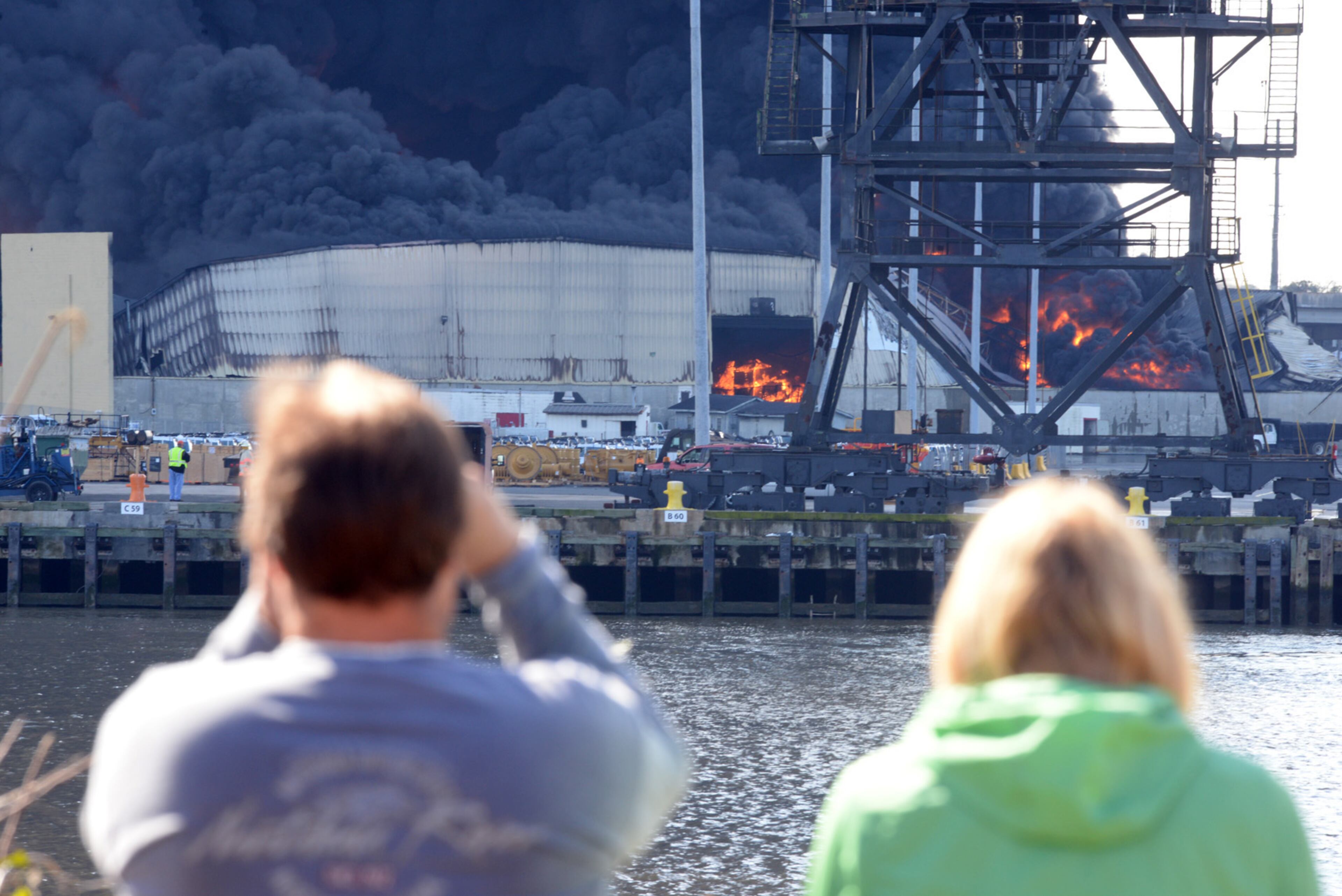 Bystanders watch from Hutchinson Island as a fire rages thorugh Ocean Terminal Warehouse No.3 at the Georgia Ports Authority on Saturday, Feb. 8, 2014.. Burning rubber from the fire at the Port of Savannah sent up a towering column of black smoke that could be seen from miles away. The cause of the fire wasn't immediately known, but all port workers were accounted for and unharmed.(AP Photo/Savannah Morning News, Richard Burkhart)