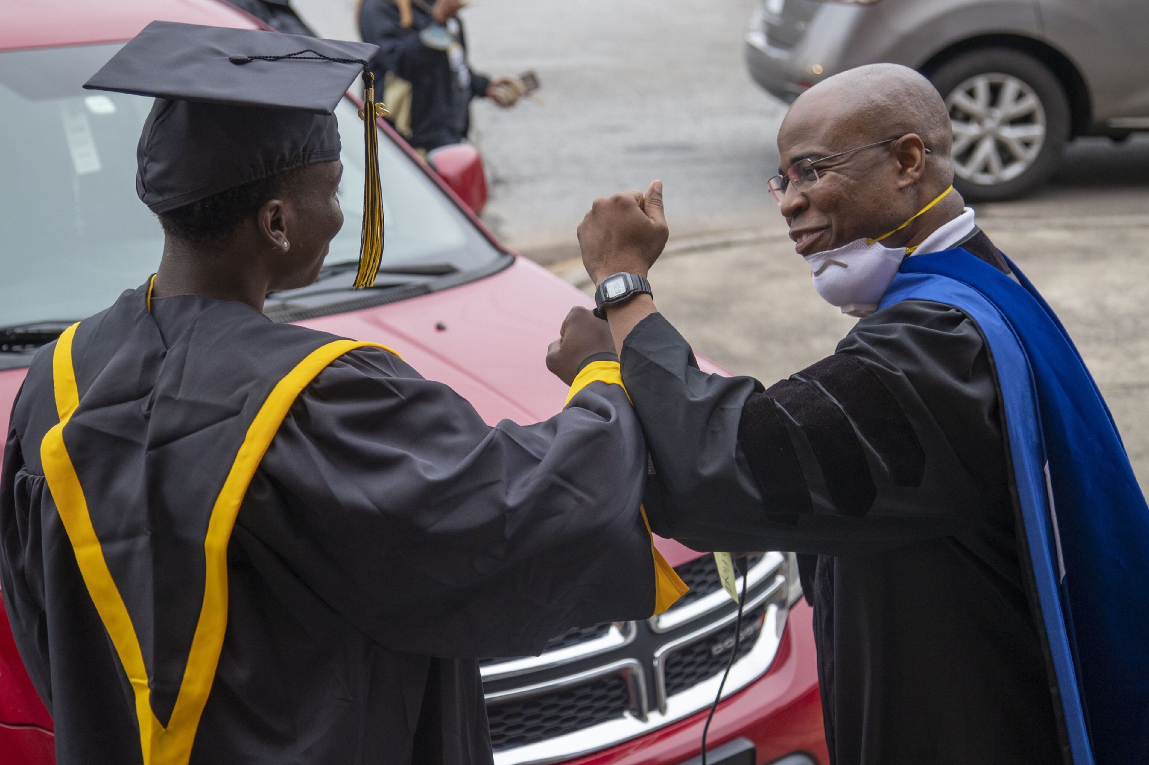 Frederick Douglass High School principal Ellis Duncan (right) congratulates a graduating senior with an elbow bump during a drive-thru celebration event at the school in Atlanta's Center Hill community, Wednesday, May 20, 2020. Graduating seniors were given their diplomas, cap, gowns and academic and athletic awards during the drive-thru event at the school. Students were also given a chance to be photographed win their cap and gown which was provided by the Frederick Douglass High School Alumni Association.