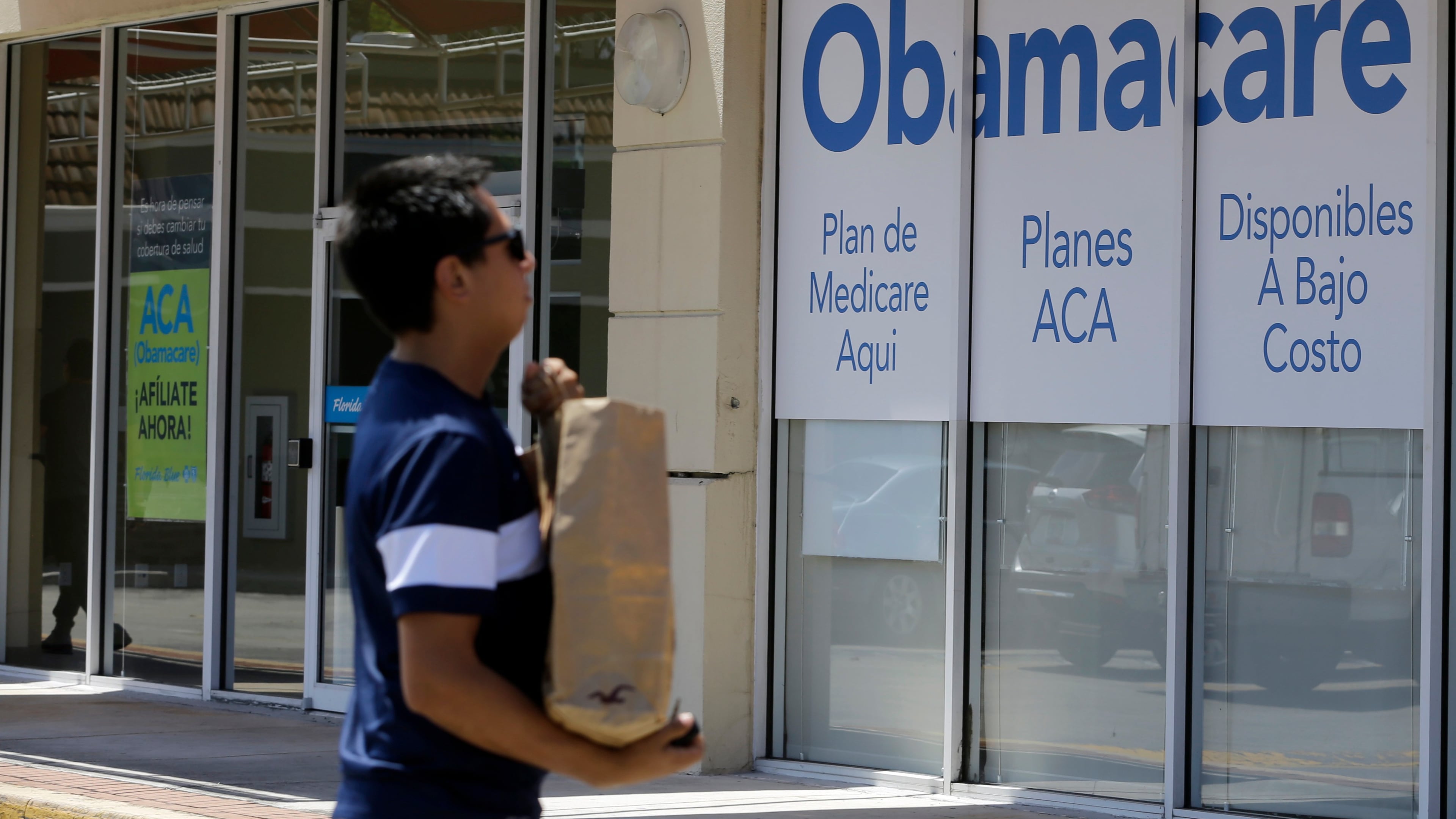 FILE - A man walks by an healthcare insurance office in Hialeah, Fla., July 27, 2017, (AP Photo/Alan Diaz, File)