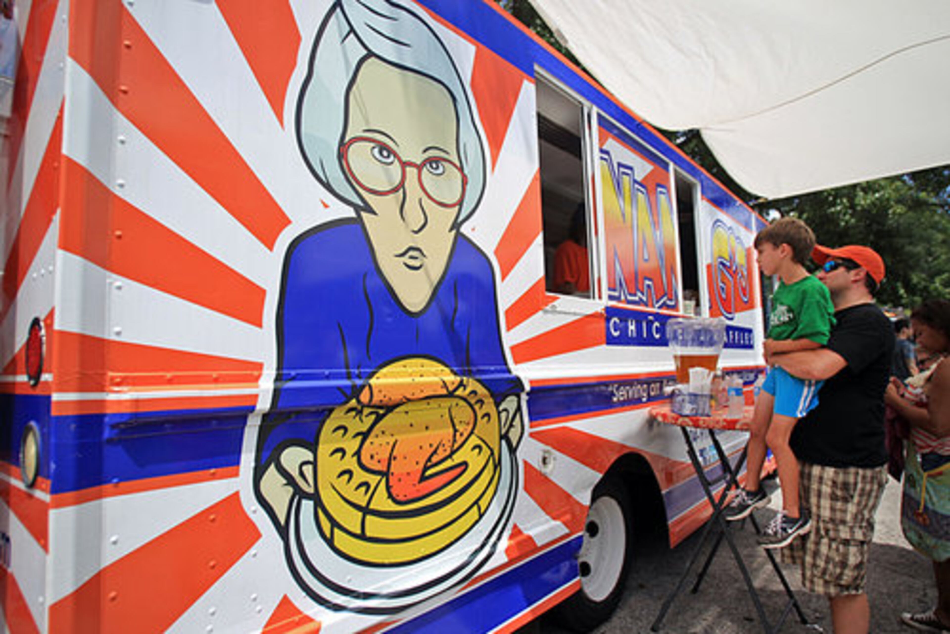 Scott Brady, of Decatur, holds up his eight-year-old son Will so he can look inside the Nang's Chicken & Waffle food truck as they wait for their lunch.