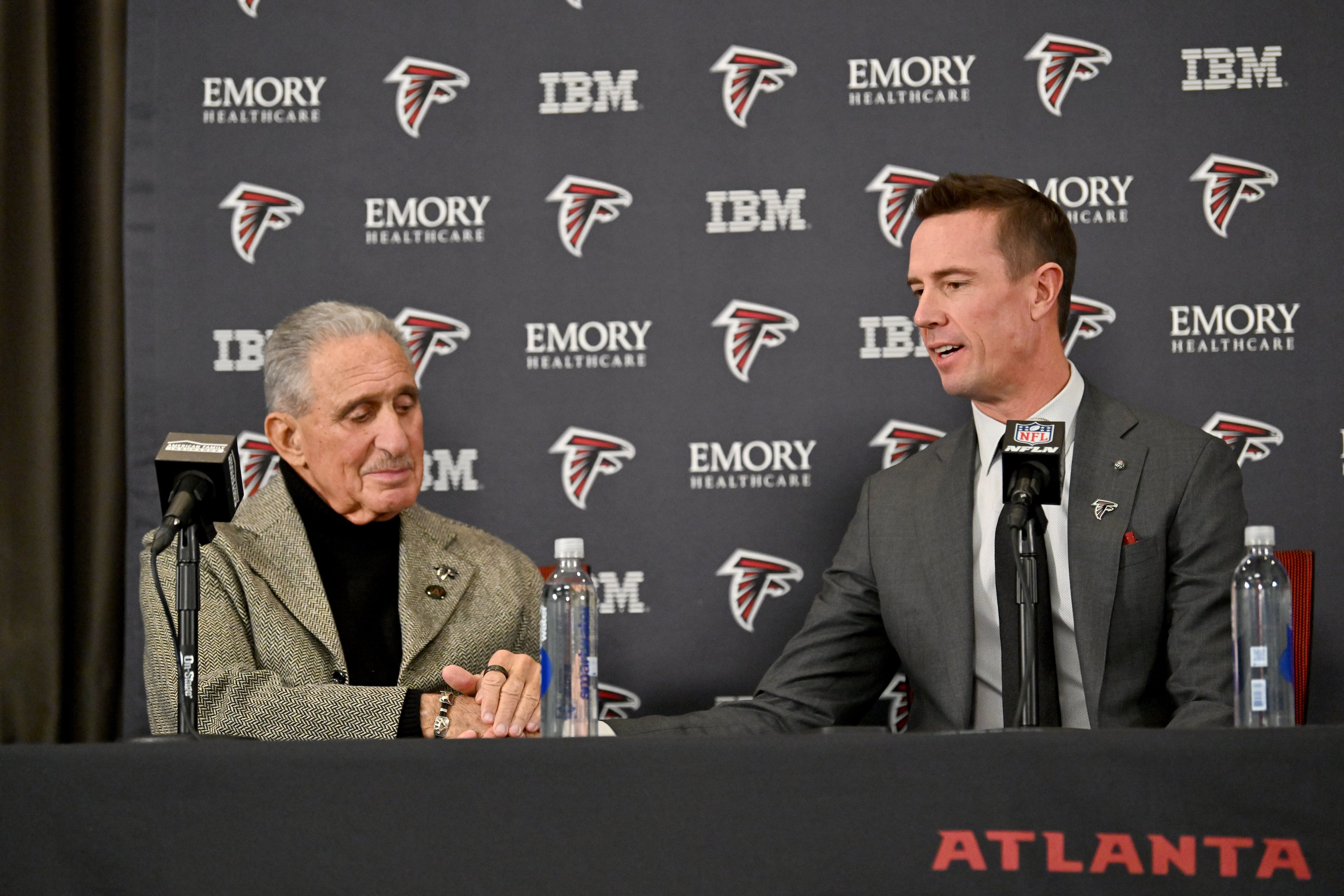 Atlanta Falcons owner Arthur Blank holds a hand of new Atlanta Falcons president of football Matt Ryan as he speaks to members of the press during a news conference to introduce new Falcons president of football Matt Ryan, Tuesday, Jan. 13, 2026, in Flowery Branch. (Hyosub Shin/AJC)