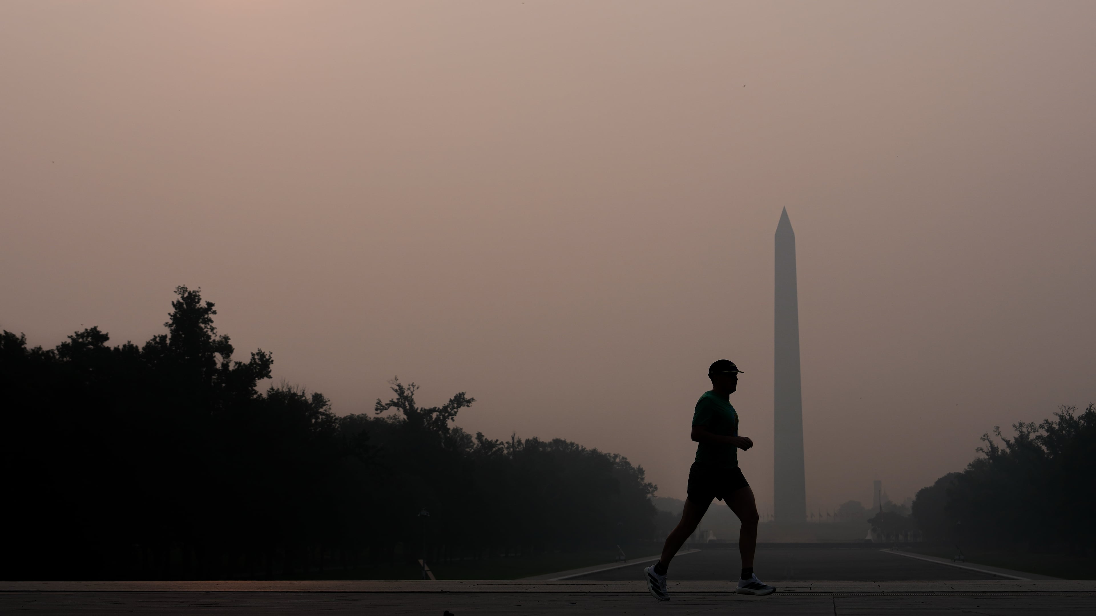 The sun is obscured by wildfire smoke as a person runs in front of the Washington Monument and Lincoln Memorial Reflecting Pool, Friday, July 17, 2026, on the National Mall in Washington. (AP Photo/Julia Demaree Nikhinson)