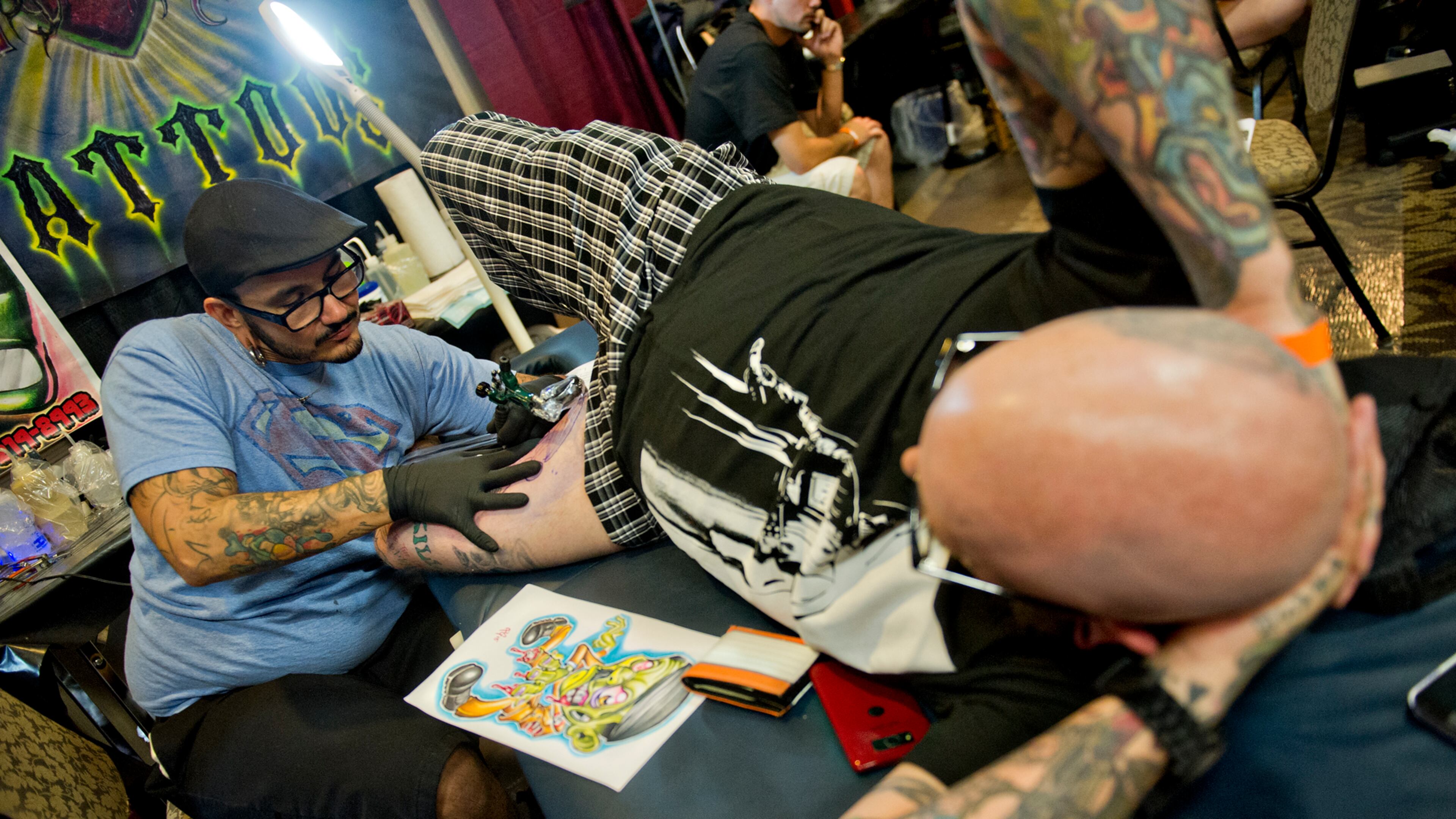 Eddy Arg (left) tattoos Chris Emory's inner thigh during the Atlanta Tattoo Expo at the Wyndham Atlanta Galleria hotel on Saturday, June 7, 2014. Close to 90 tattoo artists participated in the 18th annual three day expo.