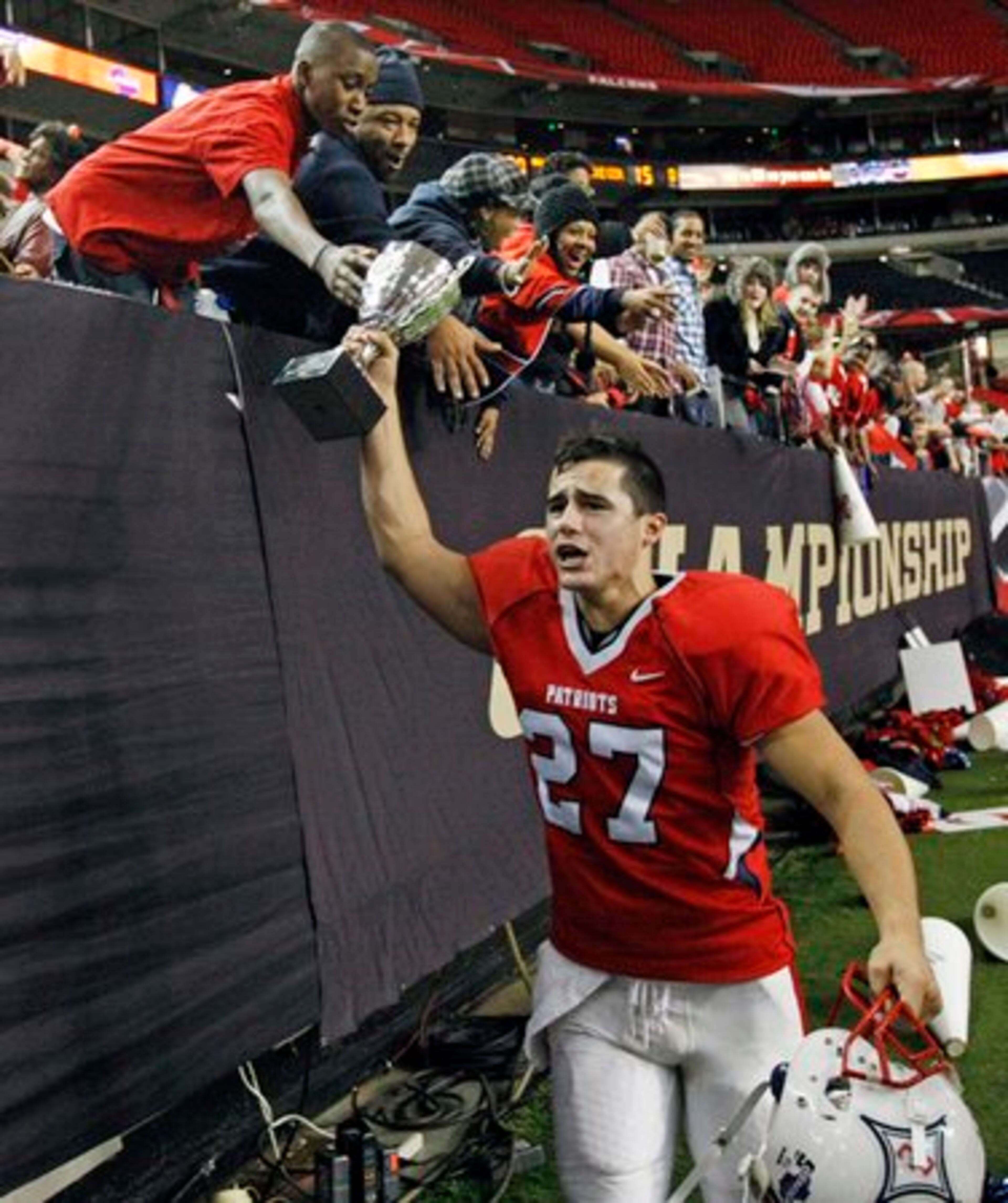 Sandy Creek kicker # 27 Zack Lopez runs down the sidelines showing off the trophy to fans.