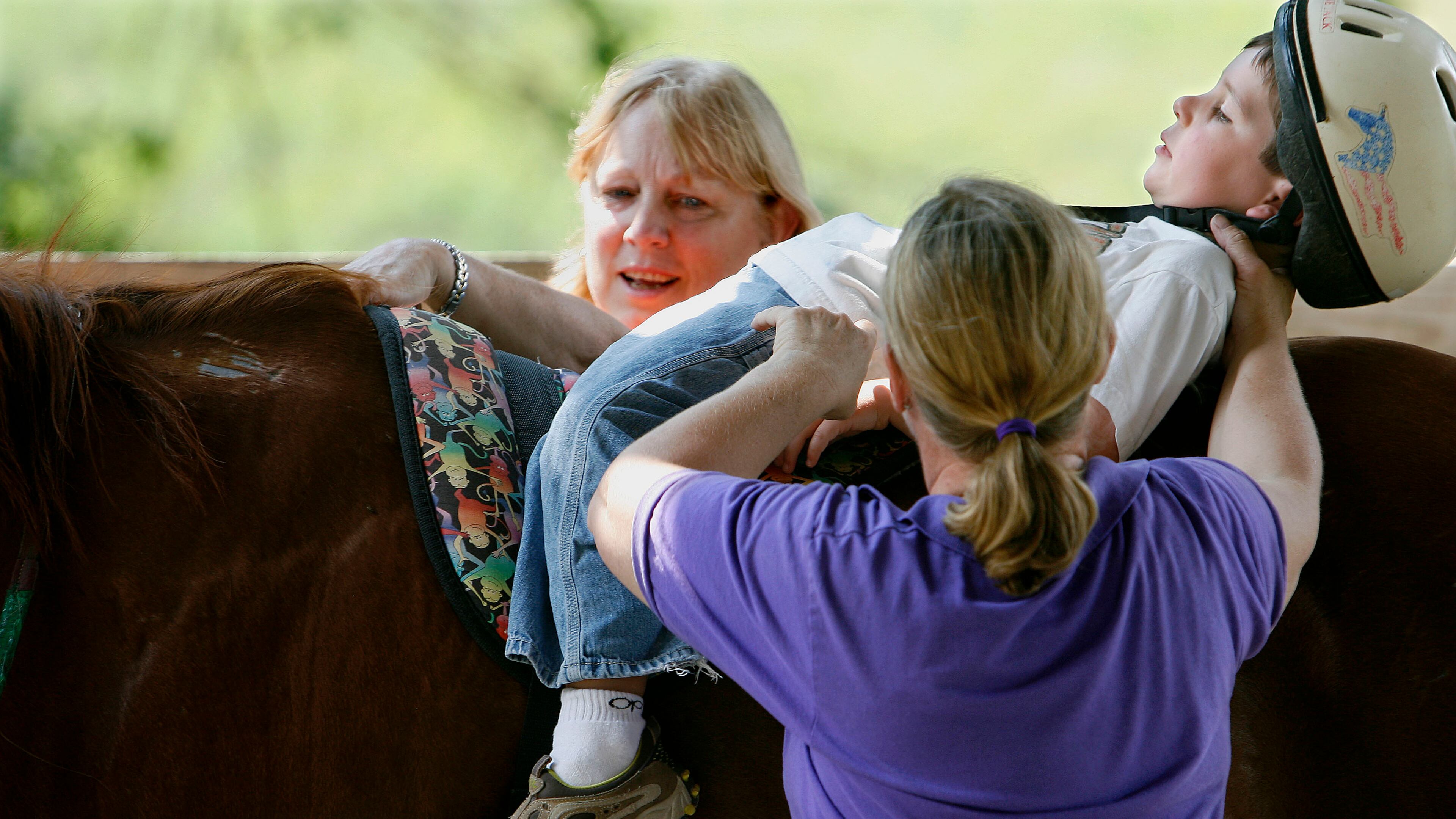 In this June 26, 2008 photo, Cole Simonds, 5 1/2, of Lilburn, rides the horse flat on his back with help from volunteer Terry Allen, left, of Lawrenceville, and Dr. Marilyn Peterson of Snellville, during a therapeutic ride at Parkwood Farms Therapy Center in Snellville. The center provides therapy for children with special needs including autism, Downs' Syndrome, Cerebral Palsy, emotional problems and learning disabilities.