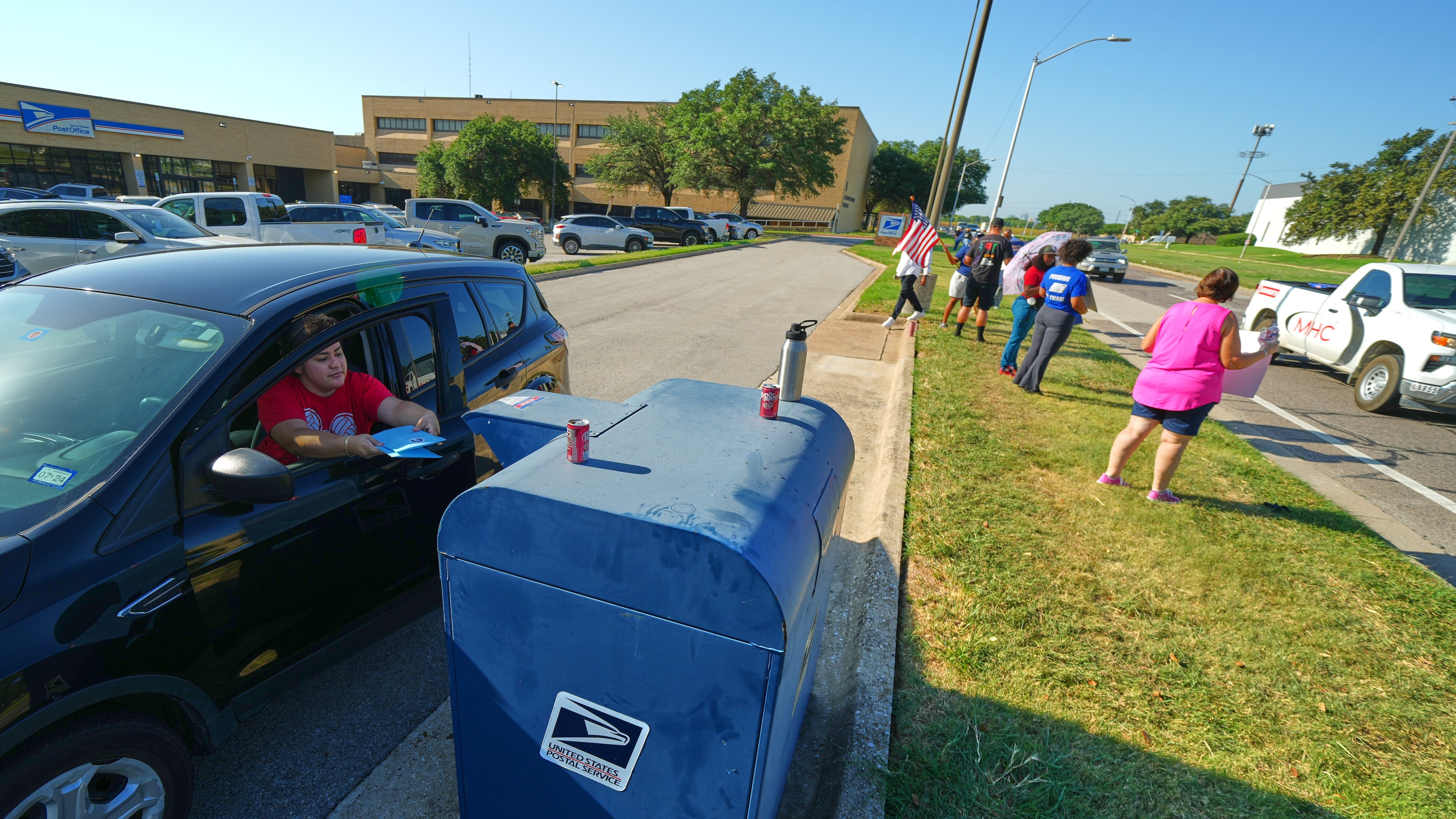 A person drops envelopes into a mailbox as postal workers participate in a national day of action outside a U.S. Post Office building, Tuesday, July 28, 2026, in Fort Worth, Texas. (AP Photo/Julio Cortez)