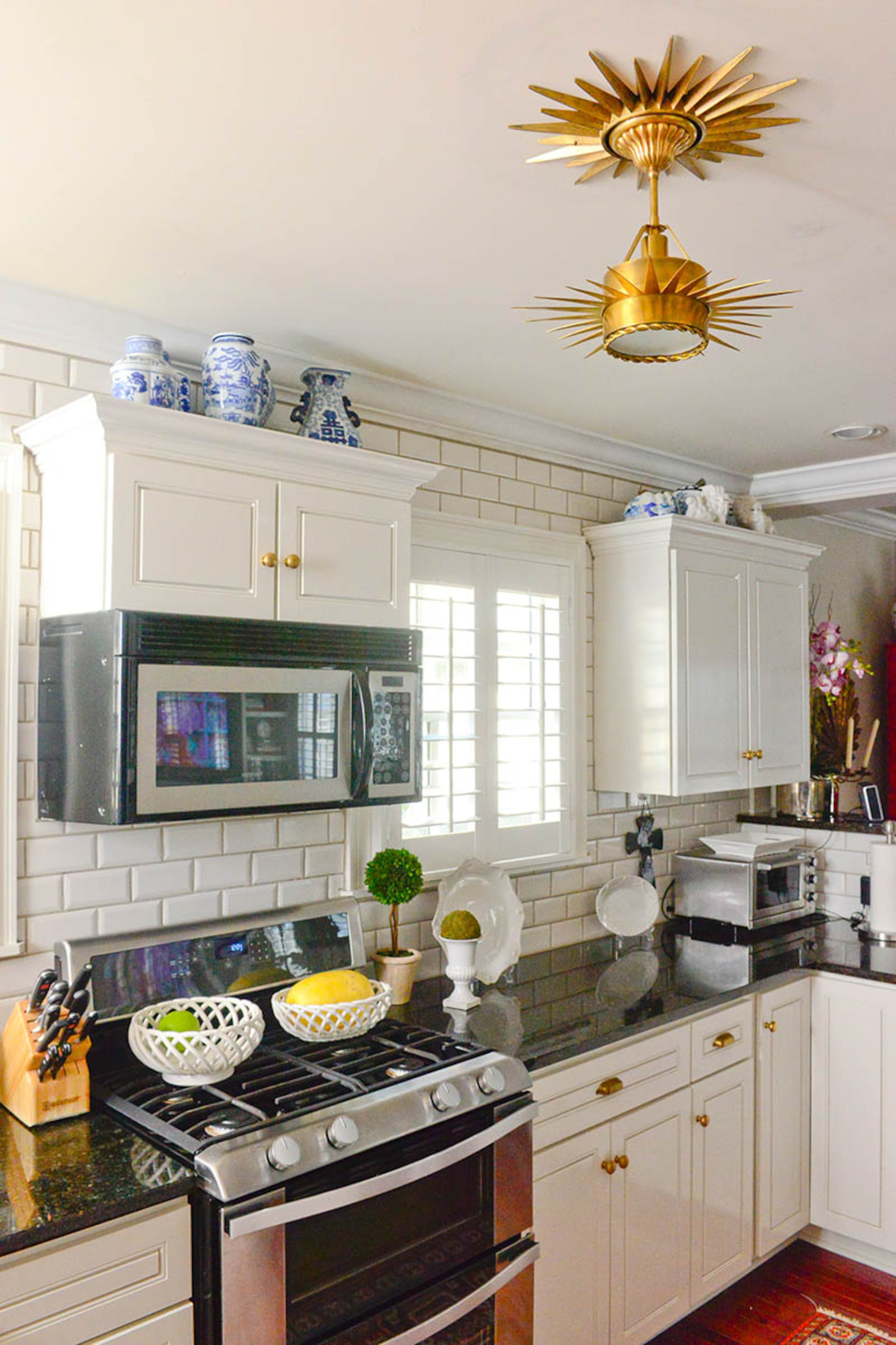 When Katie Luepke moved in to the house in 2013, she removed the center of a gold starburst mirror and placed it flush against the kitchen ceiling, giving the pendant lighting fixture from Visual Comfort an eye-catching mount. The homeowners then chose a classic white subway tile to match the traditional white cupboards.