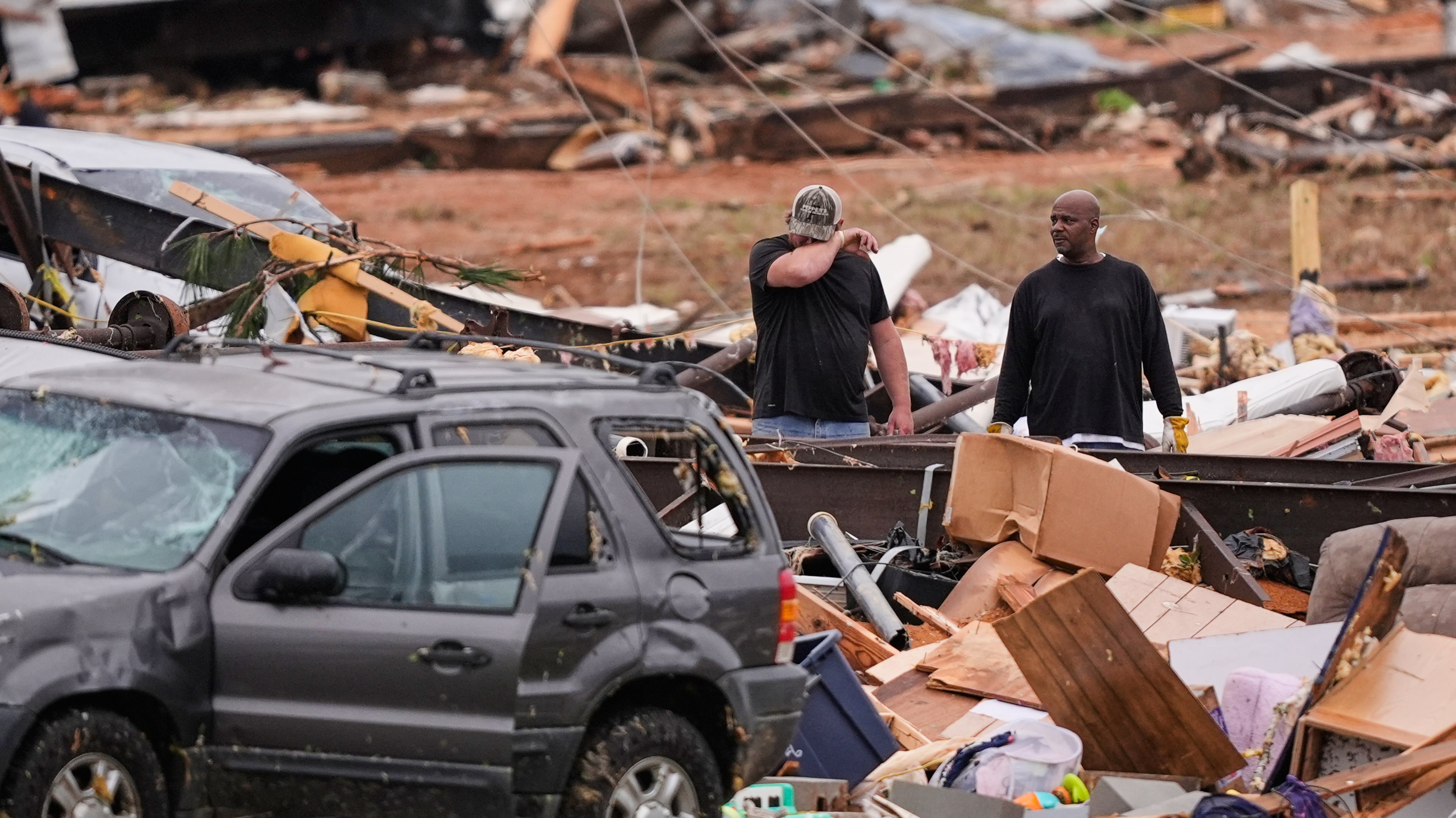 People stand among debris at Gene's Mobile Home Supply, a trailer park in Bogue Chitto, Miss., Thursday, May, 7, 2026, after a tornado cut across the state. (AP Photo/Gerald Herbert)