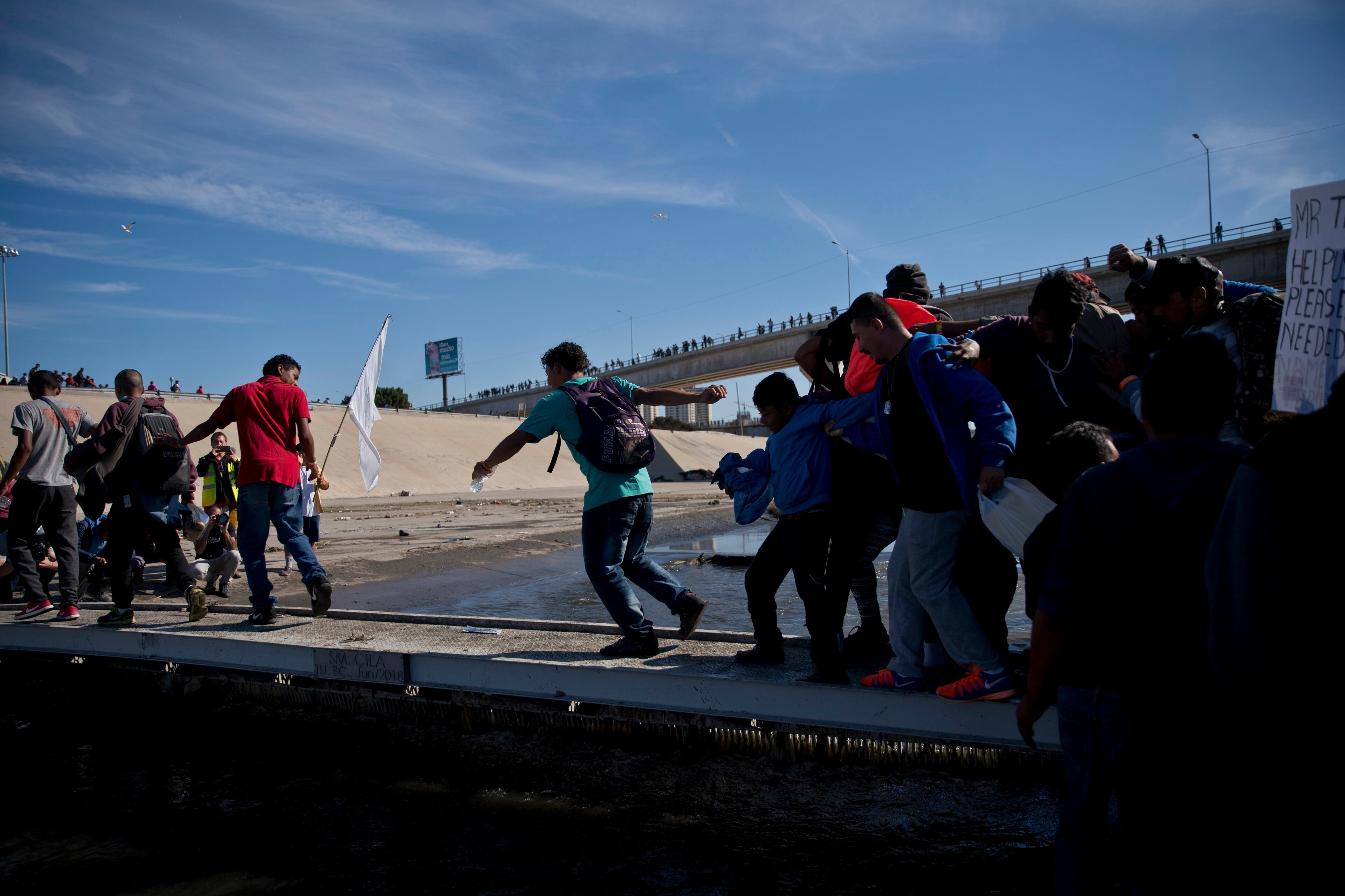 Migrants cross the river at the Mexico-U.S. border after getting past a line of Mexican police at the Chaparral crossing in Tijuana, Mexico, Sunday, Nov. 25, 2018, as they try to reach the U.S. The mayor of Tijuana has declared a humanitarian crisis in his border city and says that he has asked the United Nations for aid to deal with the approximately 5,000 Central American migrants who have arrived in the city. (AP Photo/Ramon Espinosa)
