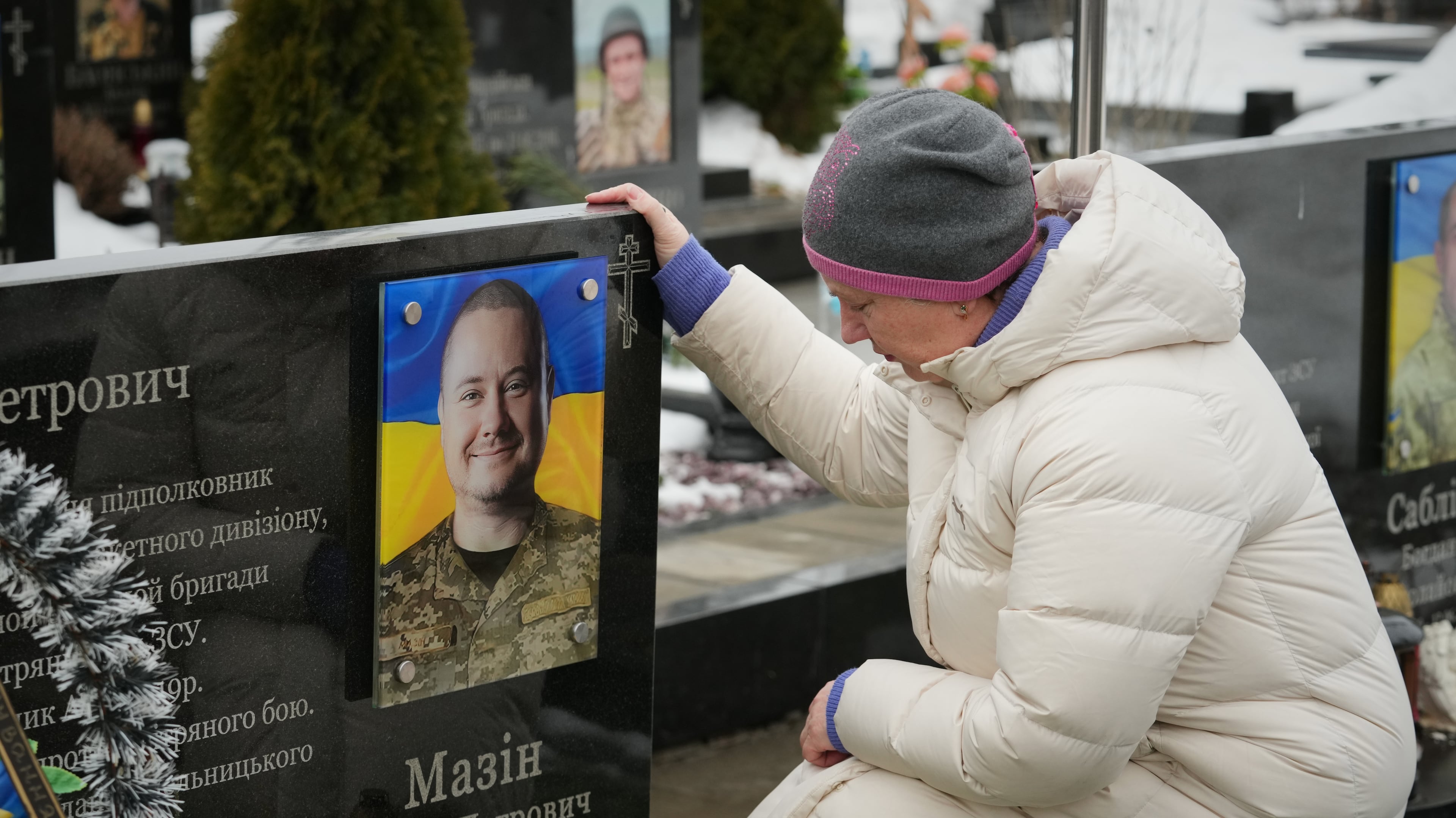 A woman sits in front of a grave of her relative during memorial service for fallen Ukrainian soldiers during a ceremony to mark the fourth anniversary of the Russian invasion of Ukraine, in Bucha, Ukraine, Tuesday, Feb. 24, 2026. (AP Photo/Sergei Grits)