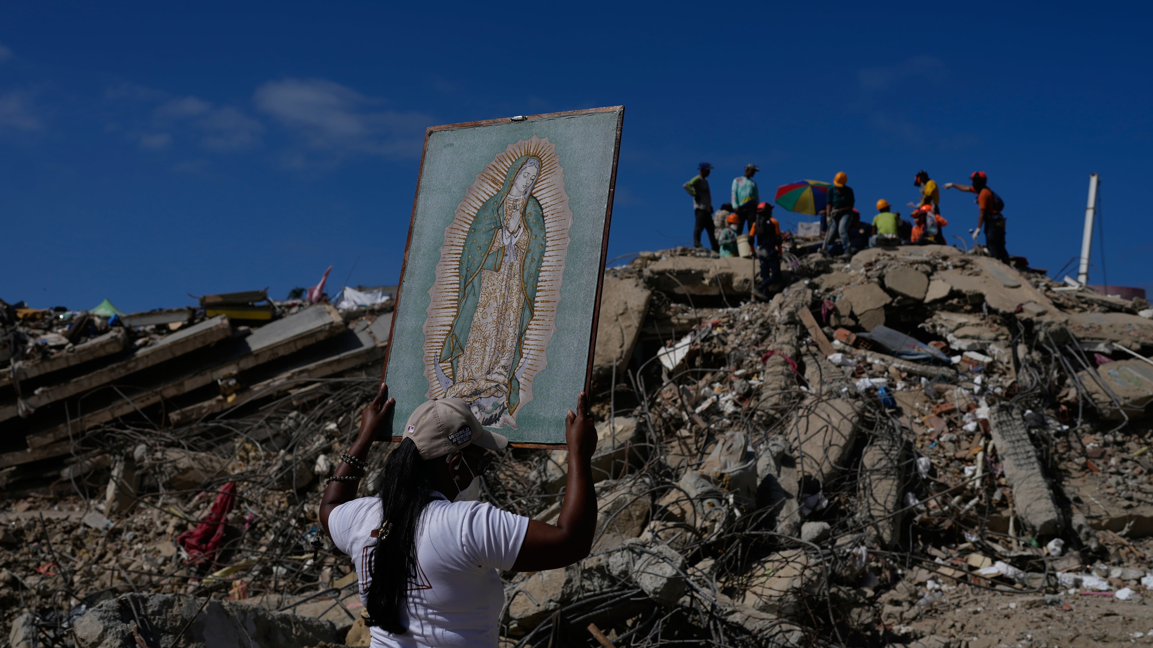 A woman holds a painting of the Virgin Mary as she accompanies a Catholic priest supporting people searching for the remains of relatives in the rubble of residential buildings that collapsed during the earthquakes that struck La Guaira, Venezuela, Friday, July 17, 2026. (AP Photo/Ariana Cubillos)