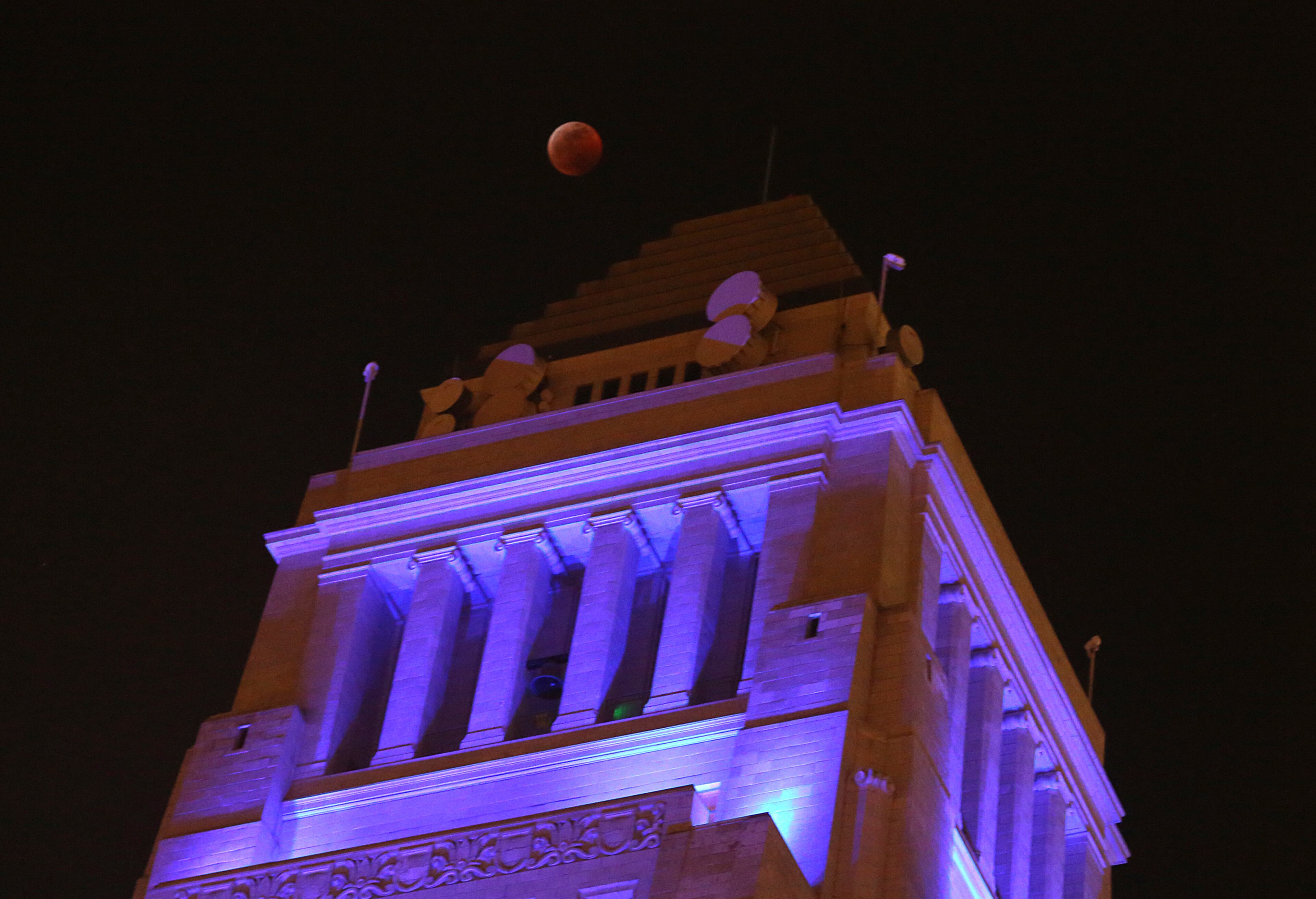 The moon, known as a supermoon due to its slightly closer proximity to Earth, is barely visible in total eclipse over Los Angeles City Hall, one of many iconic area buildings bathed in blue light in support of the L.A. Rams in their NFC championship game Sunday, Jan. 20, 2019. The eclipse came and went as predicted. The Rams defeated the New Orleans Saints and are headed to the Super Bowl. (AP Photo/Reed Saxon)