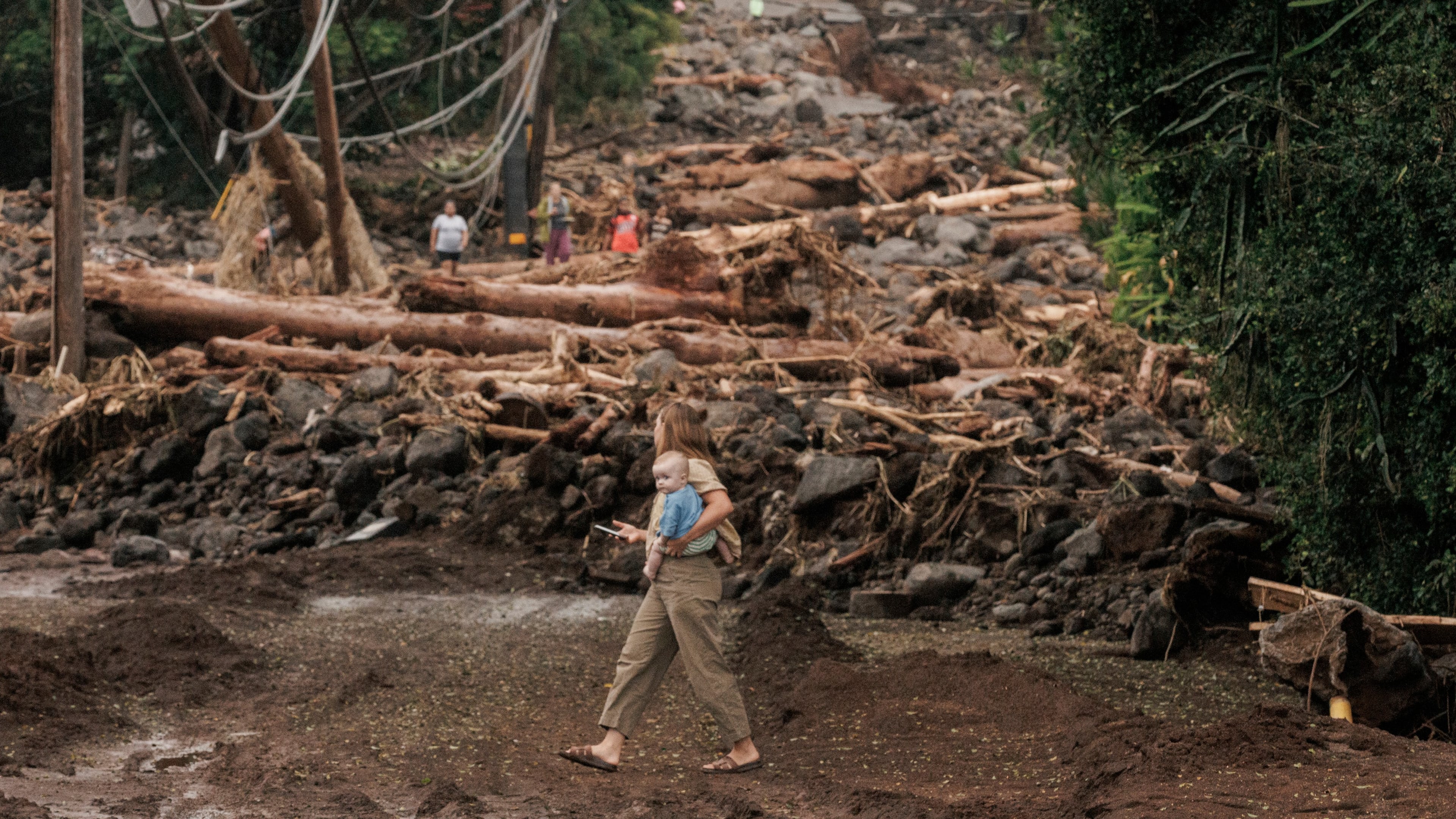 A woman and child walk past a debris-strewn street in Naalehu, Hawaii, Monday, Aug. 17, 2026, after a severe weather system went through the area. (Stephen Lam/San Francisco Chronicle via AP)
