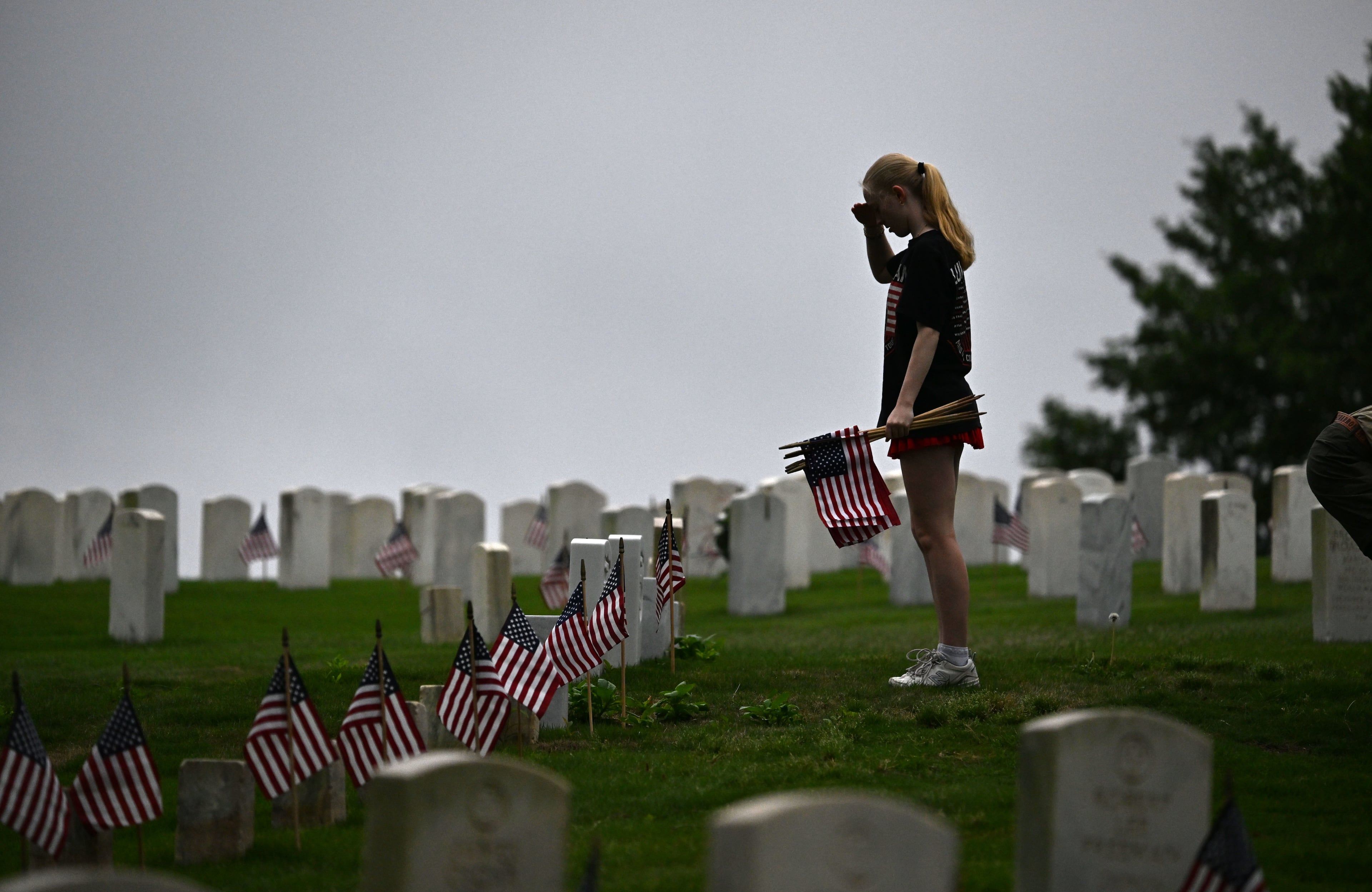 A scout salutes after placing a flag in front of a tombstone during the Memorial Day Flag Placement event at Marietta National Cemetery on Saturday, May 23, 2026, in Marietta. Scouting groups in the community place more than 18,000 U.S. veteran grave flags at Marietta National Cemetery each year on the Saturday before Memorial Day, helping prepare for Monday’s ceremony. The long-running service project—organized with the National Memorial Day Association of Georgia—also gives youth and adults an opportunity to honor fallen service members and learn about their sacrifices and the area’s history. (Hyosub Shin/AJC)