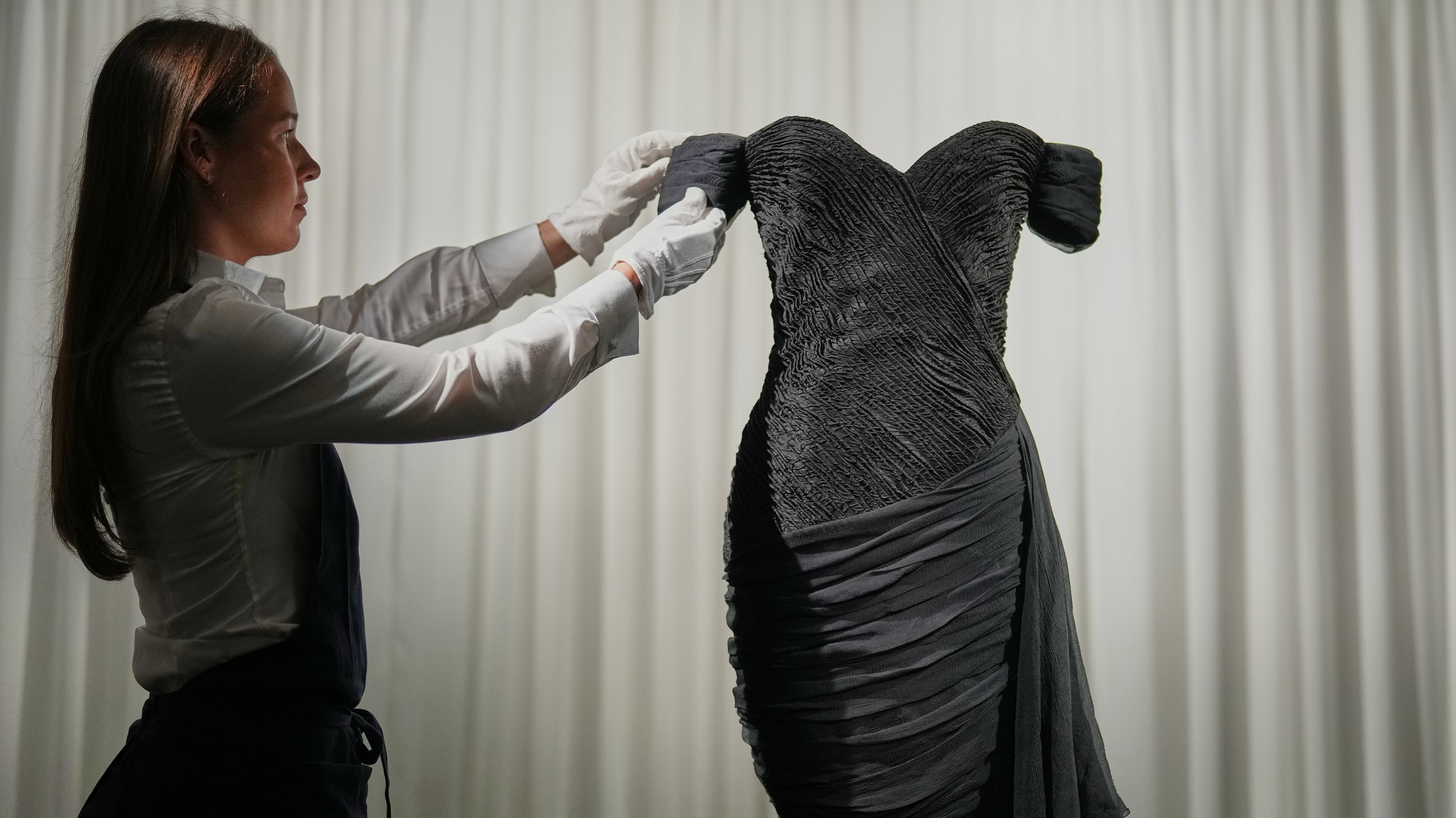 A dress worn by the late Princess Diana and known as the ''Revenge Dress'', designed by Christina Stambolian, is unveiled by staff at Sotheby’s auction house in London, Friday, Sept. 18, 2026, ahead of its Dec. 9 auction in New York, where it is estimated to sell for US$150,000-300,000. (AP Photo/Alastair Grant)