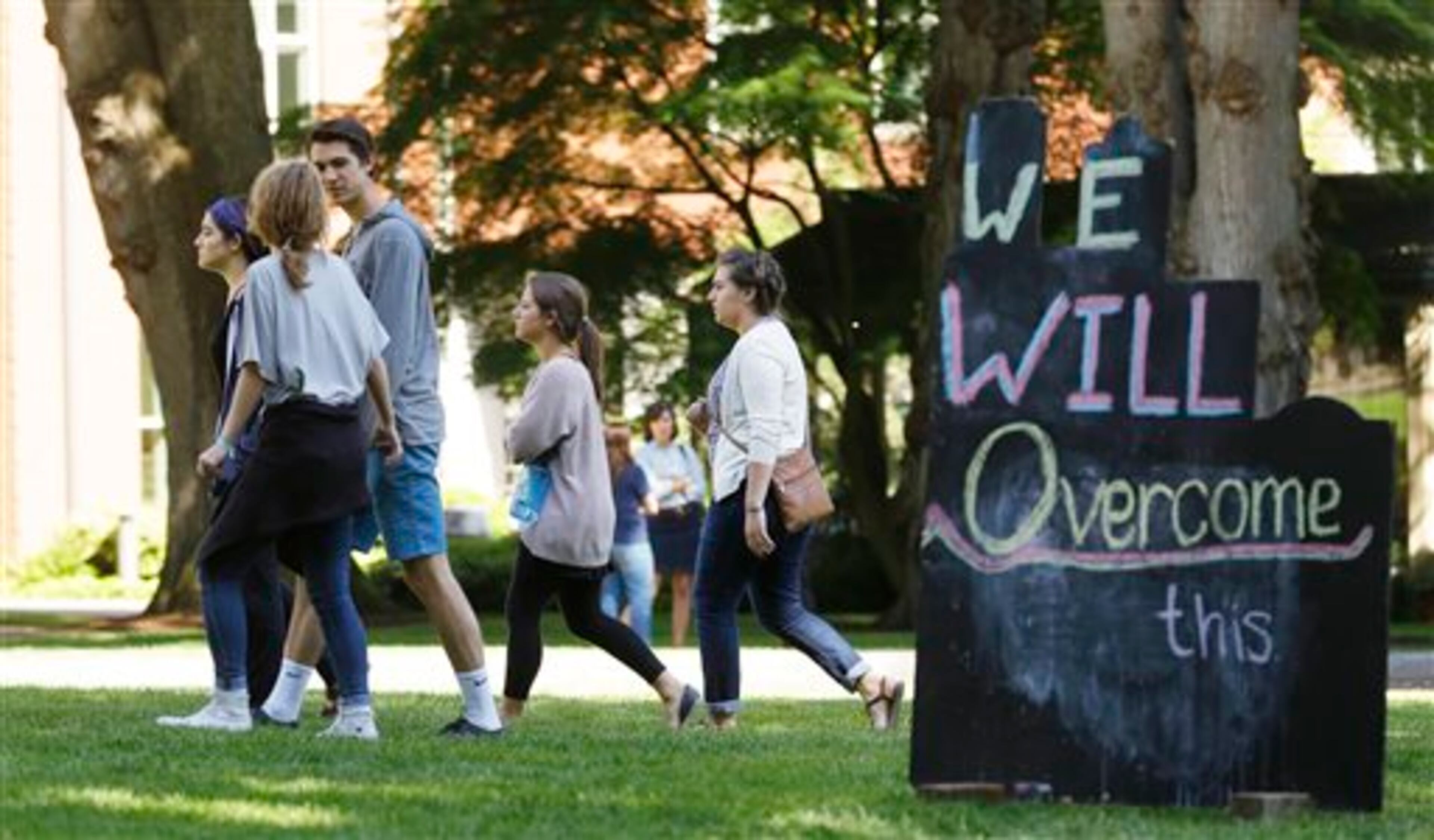 People walk past a sign on the Seattle Pacific University campus that reads "We Will Overcome This," Friday, June 6, 2014 in Seattle, the day after a shooting took place at Otto Miller Hall at the school. A 19-year-old man was fatally shot and two other young people were wounded after a gunman entered the foyer and started shooting. Aaron R. Ybarra, 26, was booked into the King County Jail late Thursday for investigation of homicide, according to police and the jail roster. (AP Photo/Ted S. Warren)