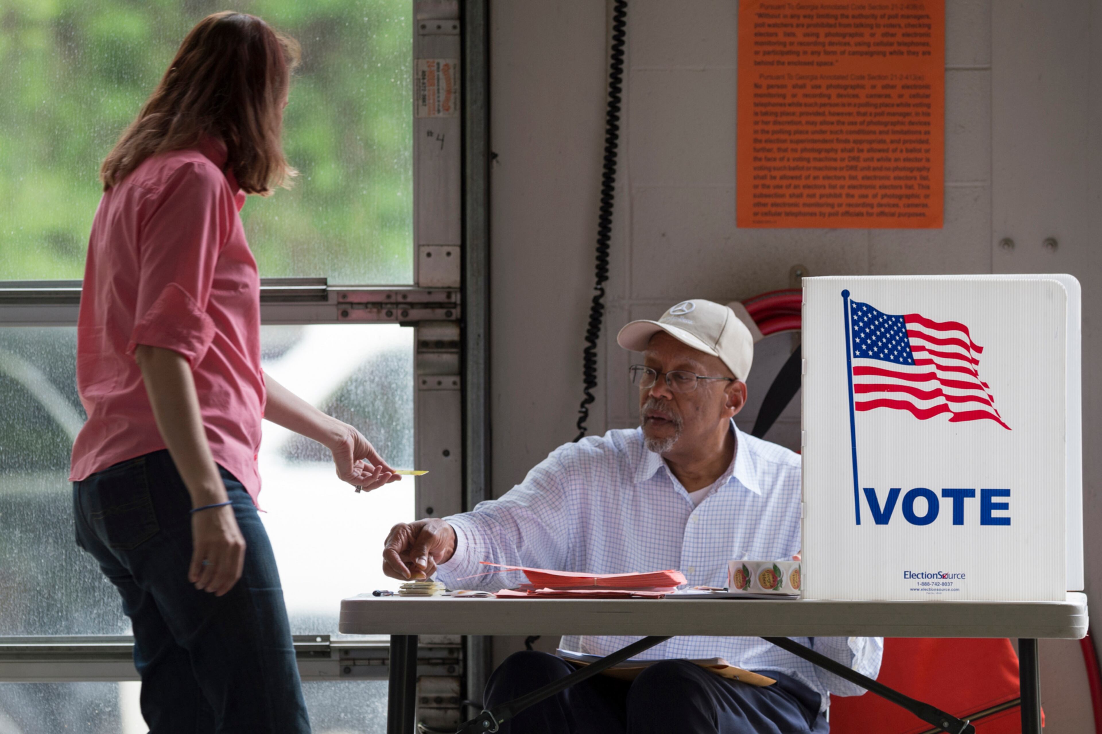 April 18, 2017, Alpharetta - Alpharetta resident Toni Kuhn, left, hands her voter card to Birdel Jackson III, center, at Alpharetta Fire Station 82 in Alpharetta, Georgia, on Tuesday, April 18, 2017. Cobb, Fulton and North DeKalb residents cast ballots today for the highly contested 6th Congressional District race. (DAVID BARNES / DAVID.BARNES@AJC.COM)