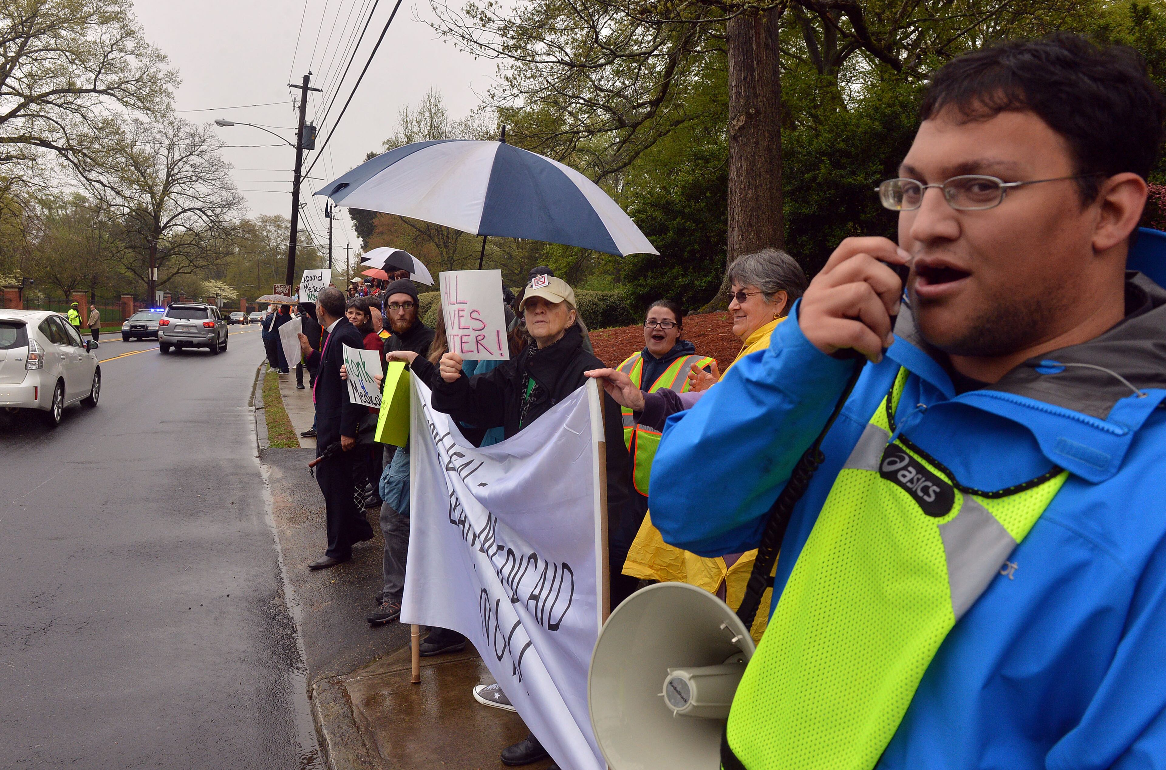 Neil Sordana uses a megaphone to chant with protesters. About 75 protesters including several Atlanta clergy members and officials joined with Moral Monday in a Medicaid expansion protest outside the Governor's Mansion on W. Paces Ferry Road Monday, April 7, 2014. Protesters were calling on Governor Nathan Deal to expand Medicaid services in the state. KENT D. JOHNSON / KDJOHNSON@AJC.COM