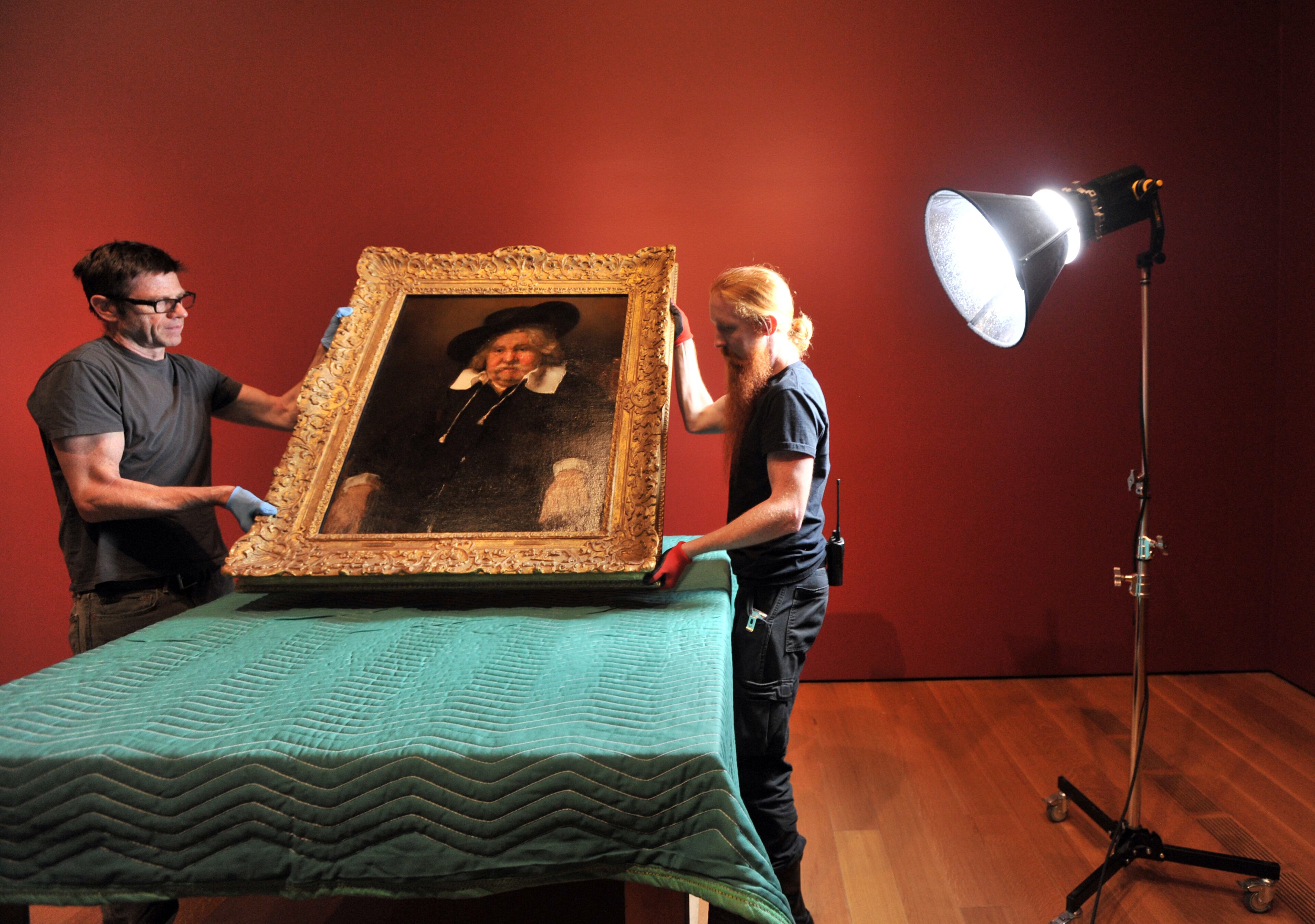 Preparators Cayse Cheatham (left) and Tommy Sapp hold one of paintings, "Portrait of an Elderly Man" ( 1667) by Rembrandt, before conducting condition reporting.