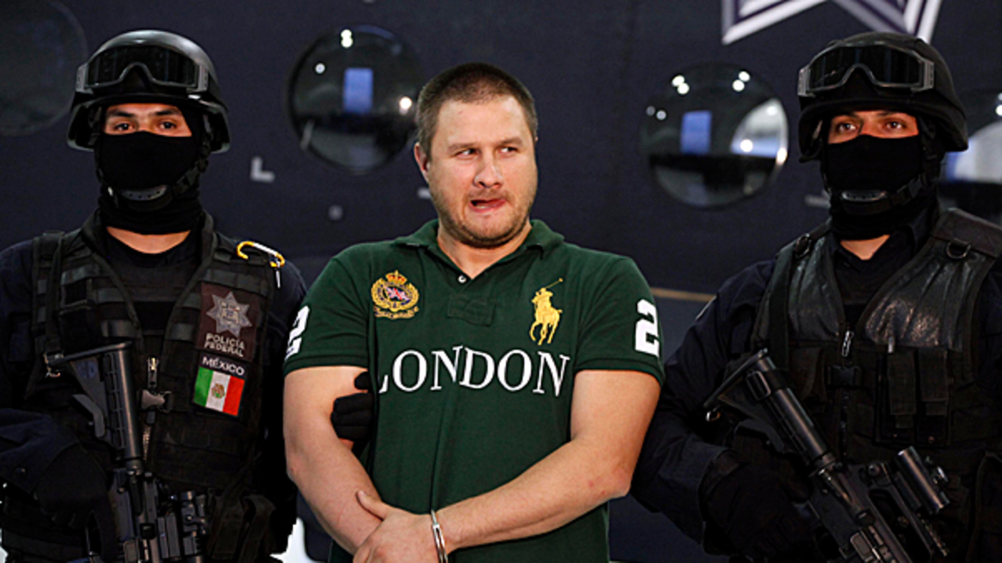 Federal police stand guard by Texas-born kingpin Edgar Valdez Villarreal, alias "the Barbie," during his presentation to the press in Mexico City, Tuesday Aug. 31, 2010. Valdez, who was captured on Monday by federal police, faces drug trafficking charges in the U.S. and has been blamed for a vicious turf war that has included bodies hung from bridges and shootouts in central Mexico.