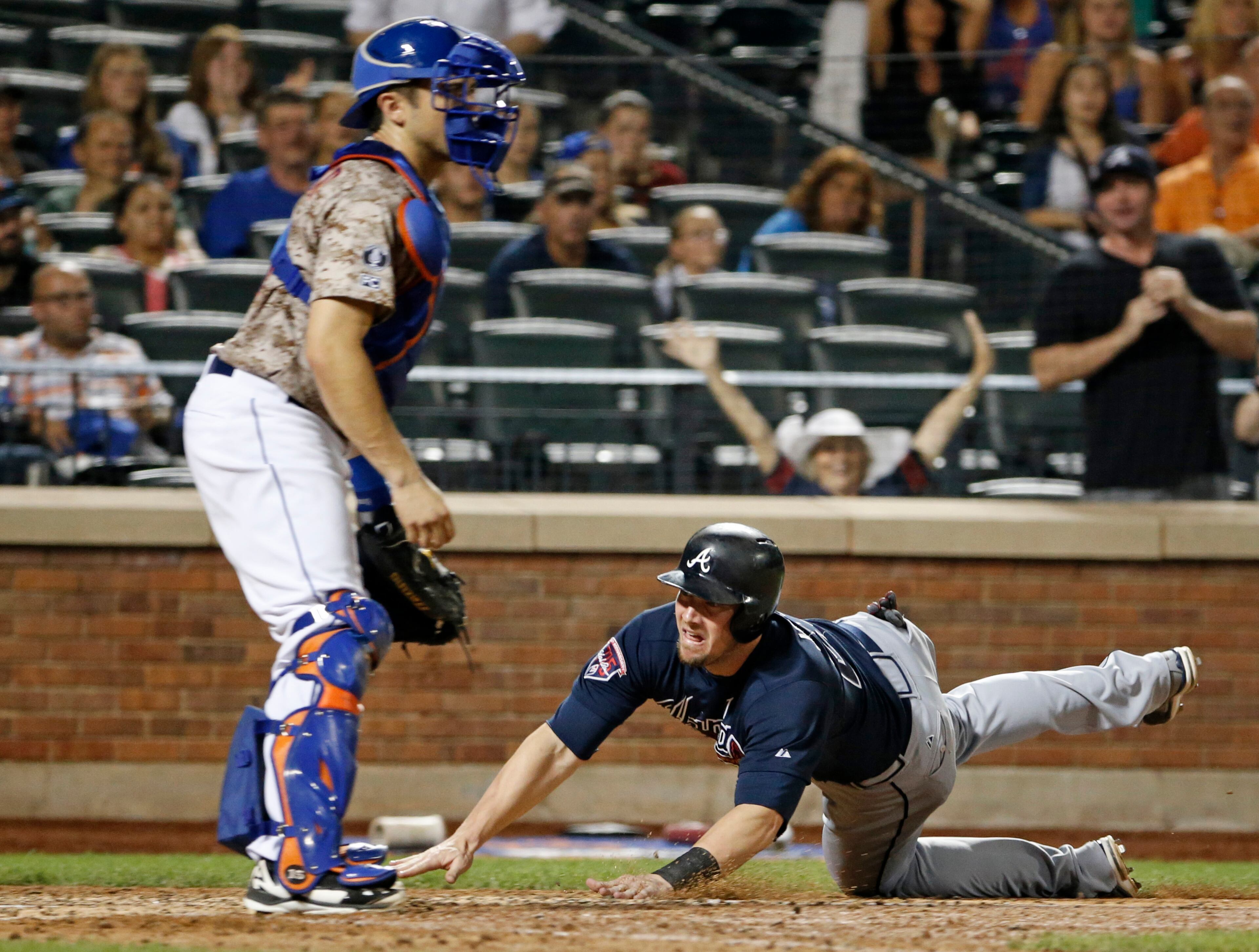 New York Mets catcher Travis d'Arnaud watches without a ball to make the tag as Atlanta Braves Chris Johnson, right, dives into the plate to score on Christian Bethancourt's eighth-inning, softly-hit RBI single in a baseball game in New York, Monday, July 7, 2014. (AP Photo/Kathy Willens)