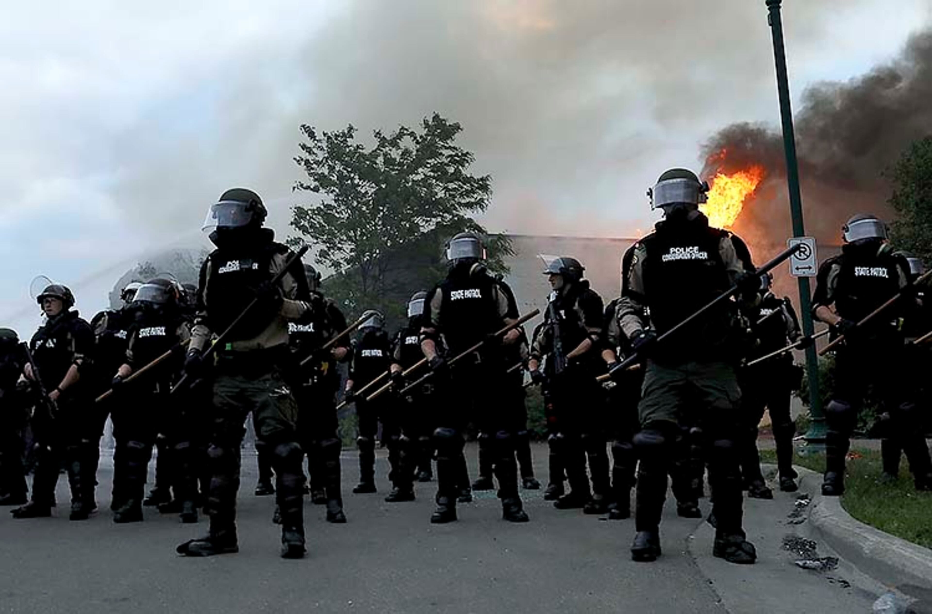 Law enforcement officers amass to protect nearby firefighters as a blaze burns along Lake St., near the Minneapolis police 3rd precinct, after a night of unrest and protests in the death of George Floyd early Friday, May 29, 2020 in Minneapolis. Floyd died after being restrained by Minneapolis police officers on Memorial Day. (David Joles/Star Tribune via AP)