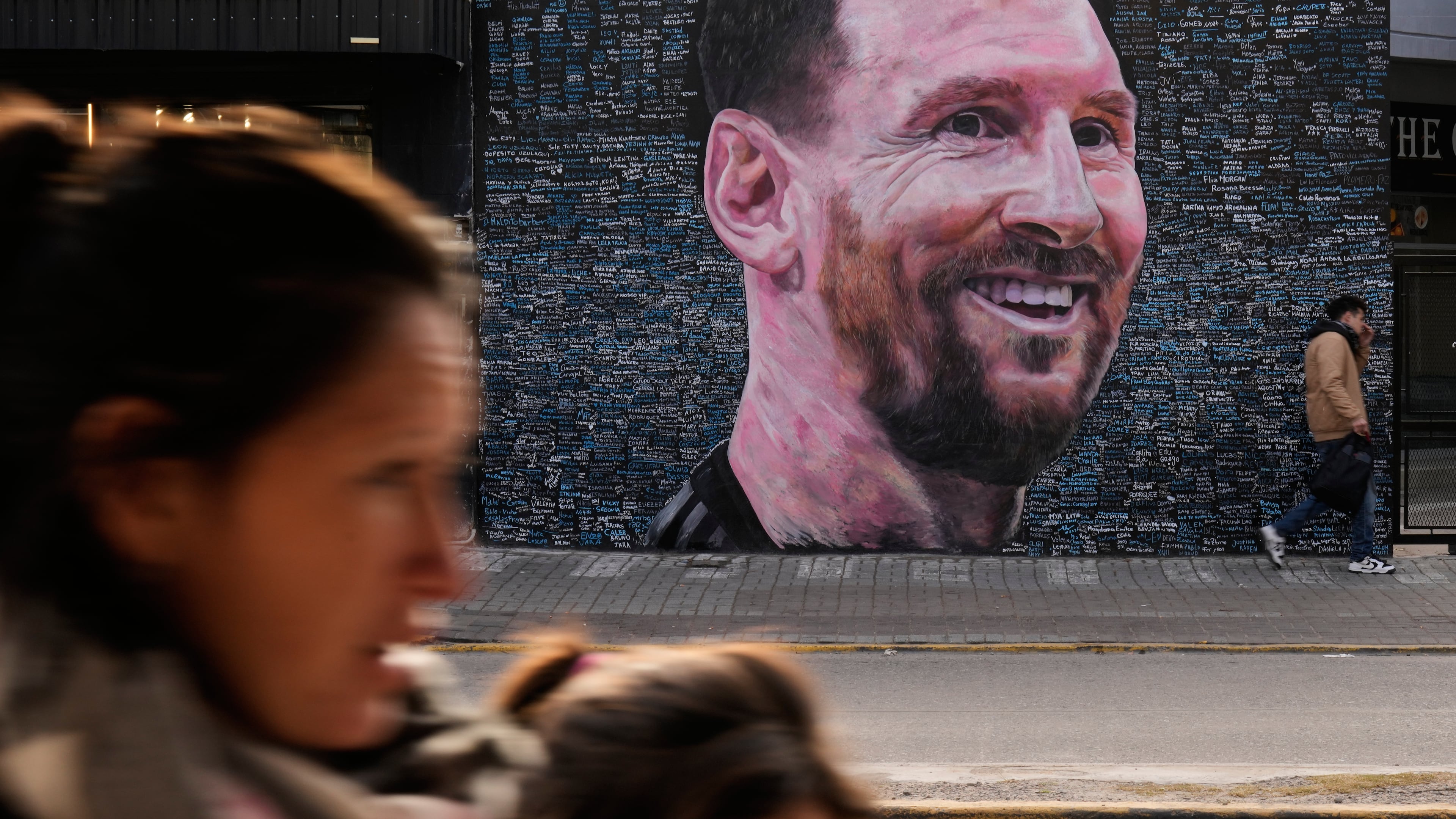 People walk past a mural of Lionel Messi by artist Leonel Garcia, which includes the names of local residents inscribed by them as a tribute to the soccer star, in Berazategui, on the outskirts of Buenos Aires, Argentina, Monday, June 22, 2026. (AP Photo/Gustavo Garello)