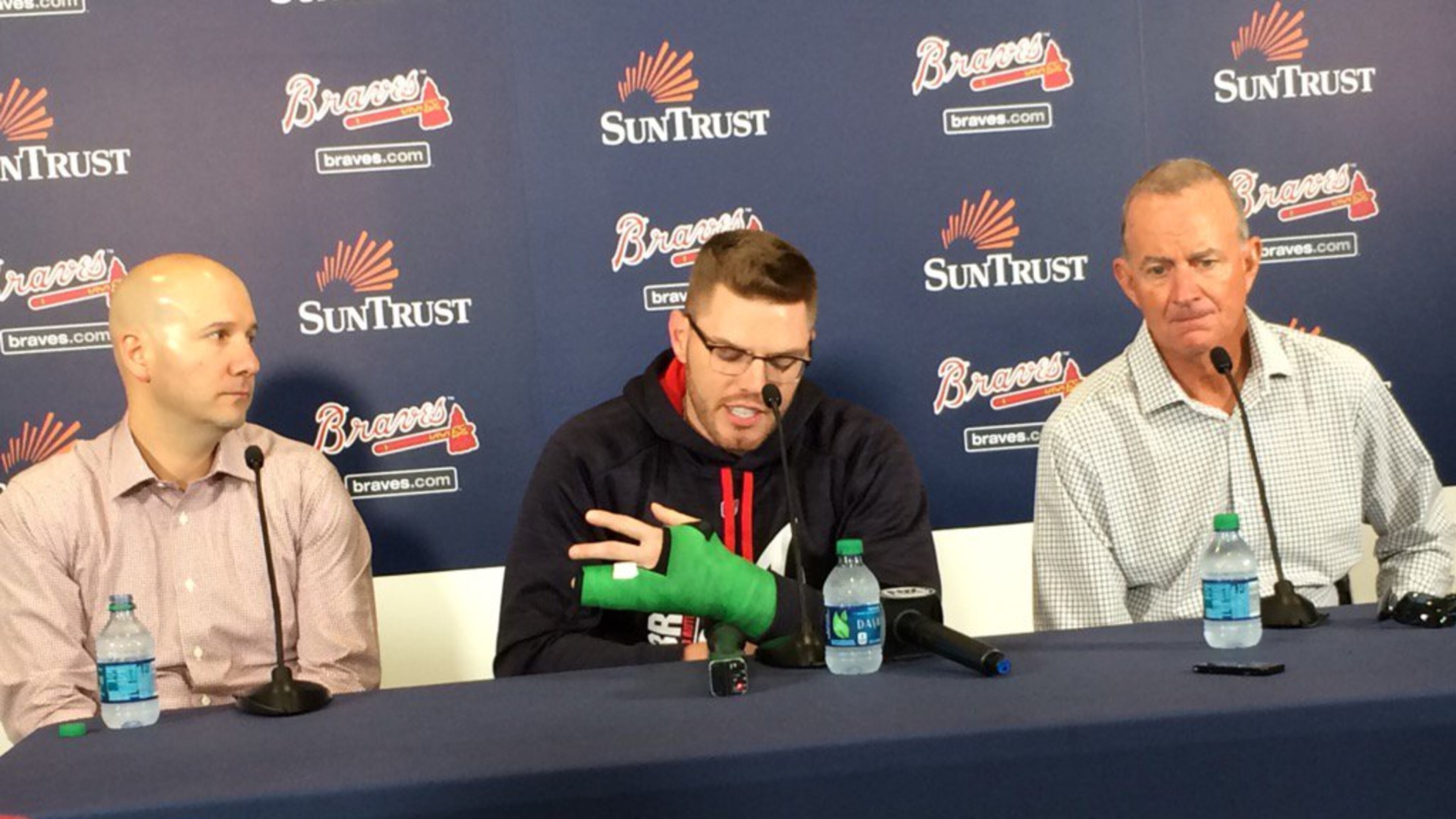 Braves first baseman Freddie Freeman, seated between general manager John Coppolella and president of baseball operations John Hart, shows the cast that protects his broken left wrist as he speaks to the media Thursday. (David O’Brien/dobrien@ajc.com)