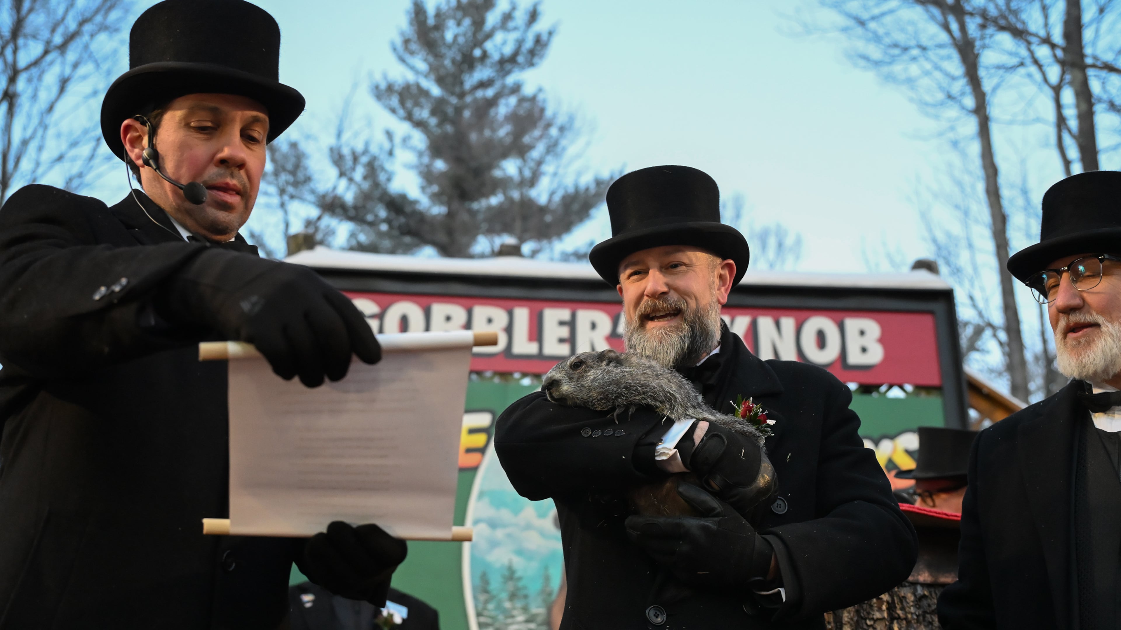 Groundhog Club Vice President Dan McGinley reads the scroll as handler A.J. Dereume holds Punxsutawney Phil, the weather prognosticating groundhog, during the 140th celebration of Groundhog Day on Gobbler's Knob in Punxsutawney, Pa., Monday, Feb. 2, 2026, Phil's handlers said that the groundhog has forecast six more weeks of winter. (AP Photo/Barry Reeger)
