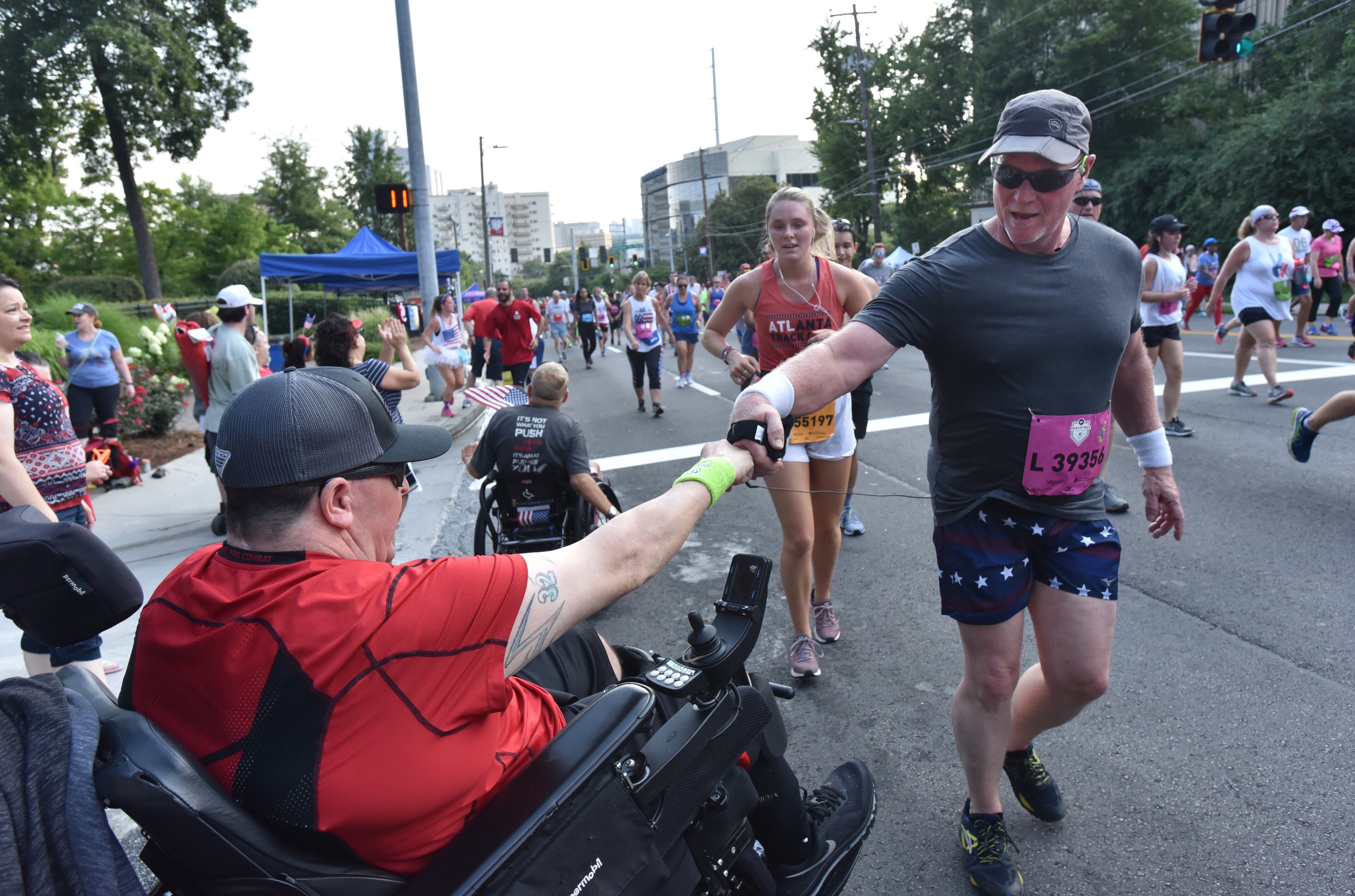 July 4, 2018 Atlanta - Ronnie Skipper (left) cheers runners with fist bump at Cardiac Hill during the AJC Peachtree Road Race on Wednesday, July 4, 2018. HYOSUB SHIN / HSHIN@AJC.COM