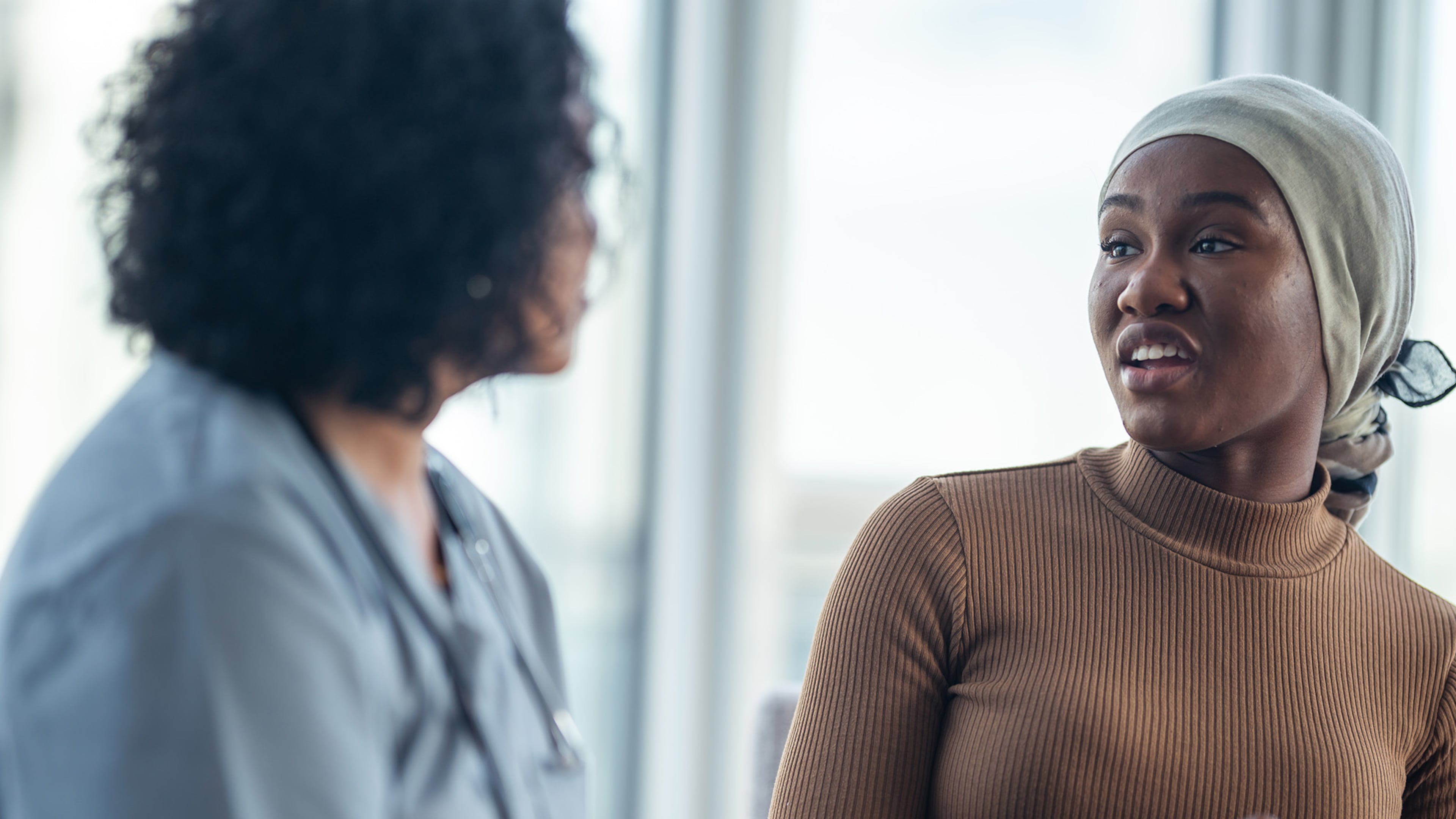 A young black woman with cancer is consulting her doctor. She is wearing a bandana to hide her hair loss. While mortality rates are declining, some cancers are more frequently diagnosed in younger Americans, and that should have us concerned.