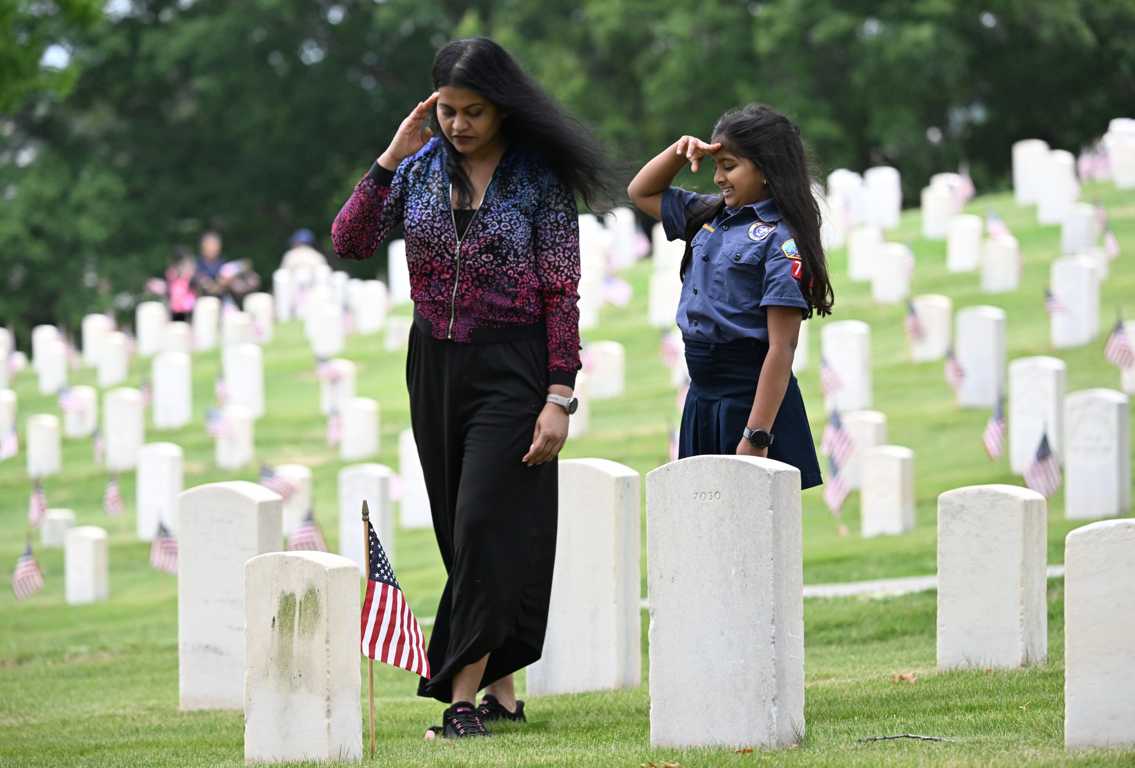 Raasya Kombiyil, right, 8, and her mother Rajani Nair salute after placing a flag in front of a tombstone during the Memorial Day Flag Placement event at Marietta National Cemetery on Saturday, May 23, 2026, in Marietta. Scouting groups in the community place more than 18,000 U.S. veteran grave flags at Marietta National Cemetery each year on the Saturday before Memorial Day, helping prepare for Monday’s ceremony. The long-running service project—organized with the National Memorial Day Association of Georgia—also gives youth and adults an opportunity to honor fallen service members and learn about their sacrifices and the area’s history. (Hyosub Shin/AJC)