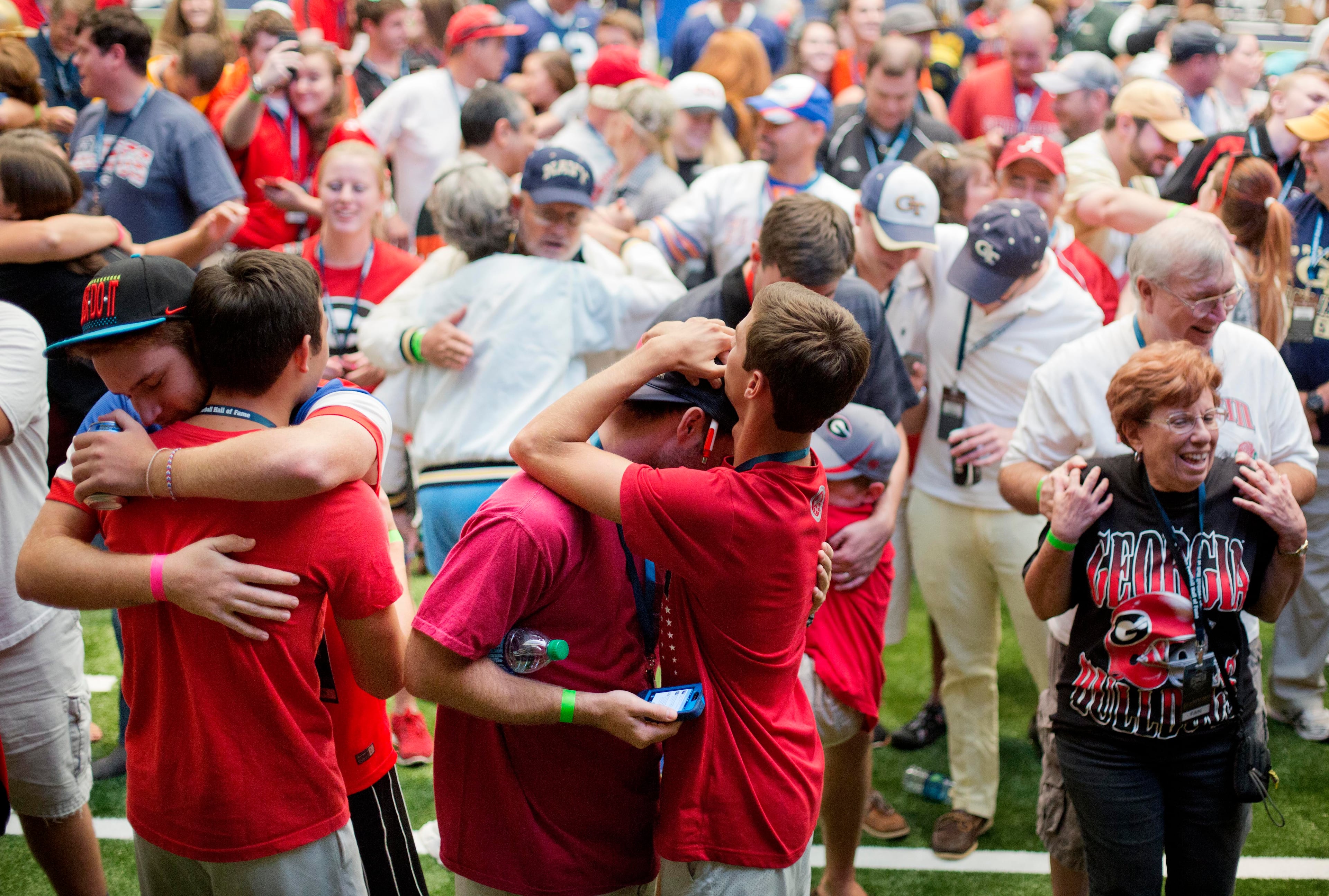 Danny Mason, from left, Nick Toomey, Walker Tuten and Matt Filer, of Atlanta, embrace as visitors are asked to hug the person next to them during a sleepover in the College Football Hall of Fame, Wednesday, Aug. 13, 2014, in Atlanta. One hundred contest winners who wrote an essay detailing their love of college football were selected to stay with a guest overnight in Atlanta's College Football Hall of Fame before its grand opening and win a year's supply of Chick-fil-A. The crowd of 200 who came from as far away as Hawaii were among the first to experience the College Football Hall of Fame and Chick-fil-A Fan experience before it opens to the public on Aug. 23. After touring the exhibits guest were served dinner on the football field before pitching their tents on the turf and settling in for the night as college football themed movies such as "Rudy" were played on the jumbotron. The hall was previously located in South Bend, Indiana, but was plagued by poor attendance. (AP Photo/David Goldman)