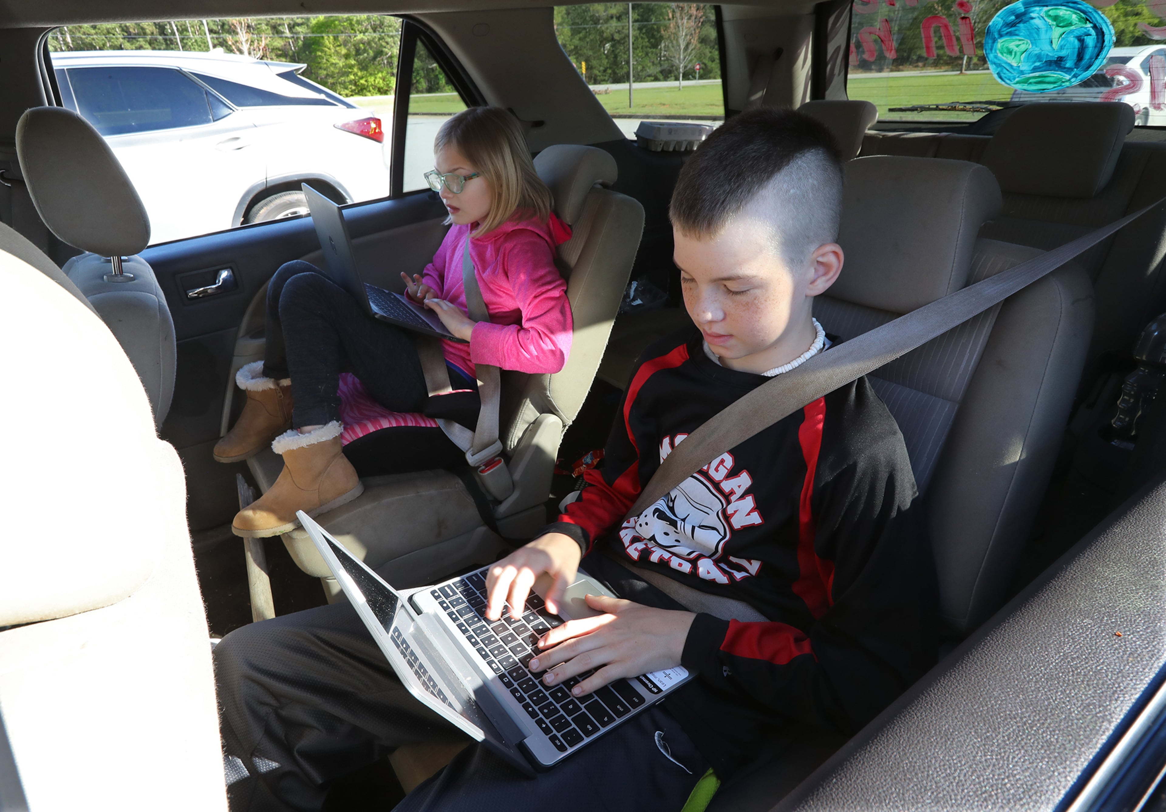 April 2, 2020 Rutledge: Home schoolers Ellis Knight, 12, and his sister Regan, 9, get their homework done in the back seat of the car after their mother Jamie Knight drove them to Union Springs Baptist Church on Thursday, April 2, 2020, in Rutledge. The biggest obstacle to distance learning is finding Wifi. Morgan County has a low-income student population and not every home has internet access. So the school district asked the local church to be a hot spot. Curtis Compton ccompton@ajc.com