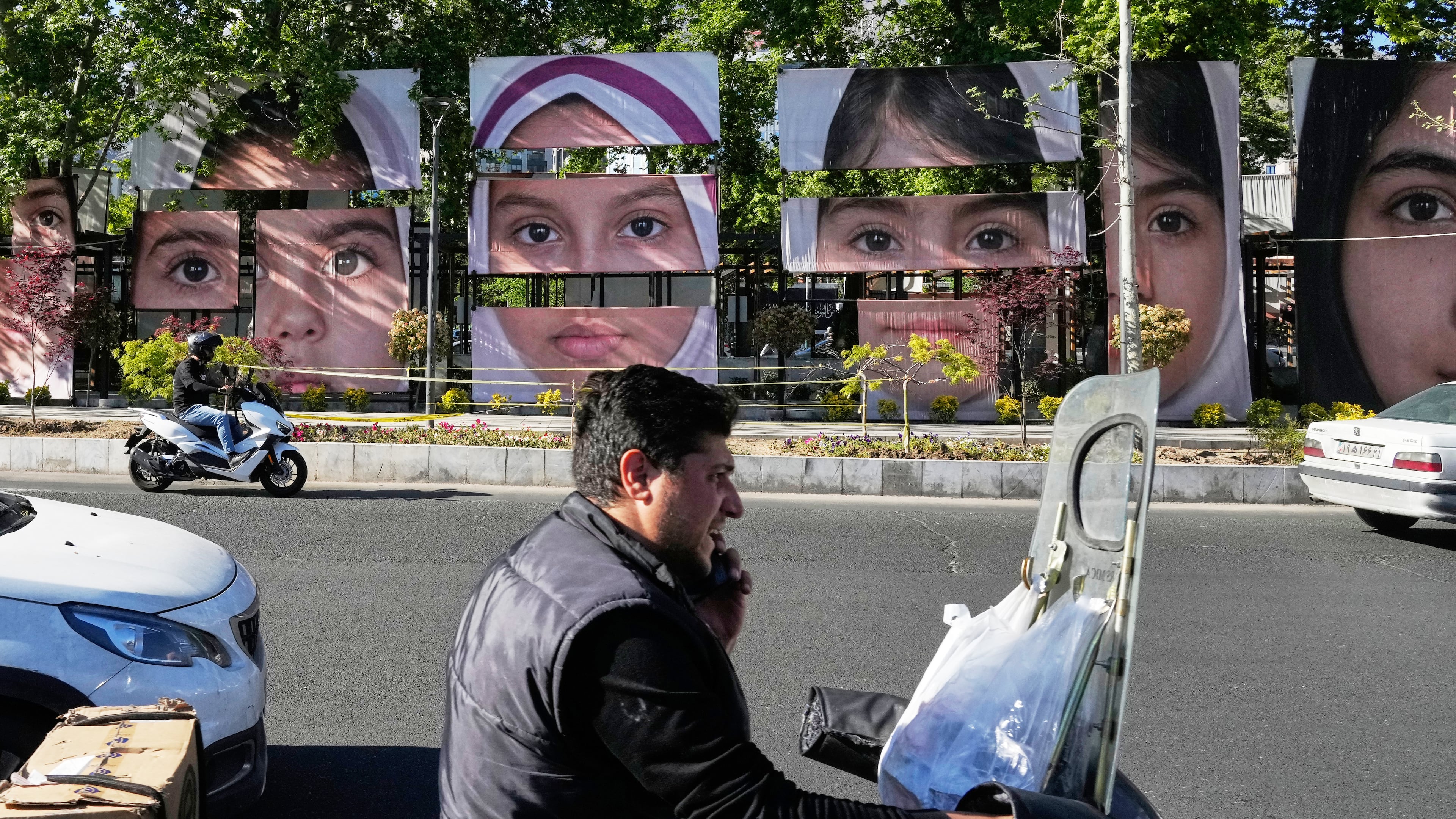 Vehicles drive past banners showing portraits of the school children who were killed during a strike on a school in southern town of Minab on Feb. 28, at Tajrish square in northern Tehran, Iran, Sunday, May 10, 2026. (AP Photo/Vahid Salemi)